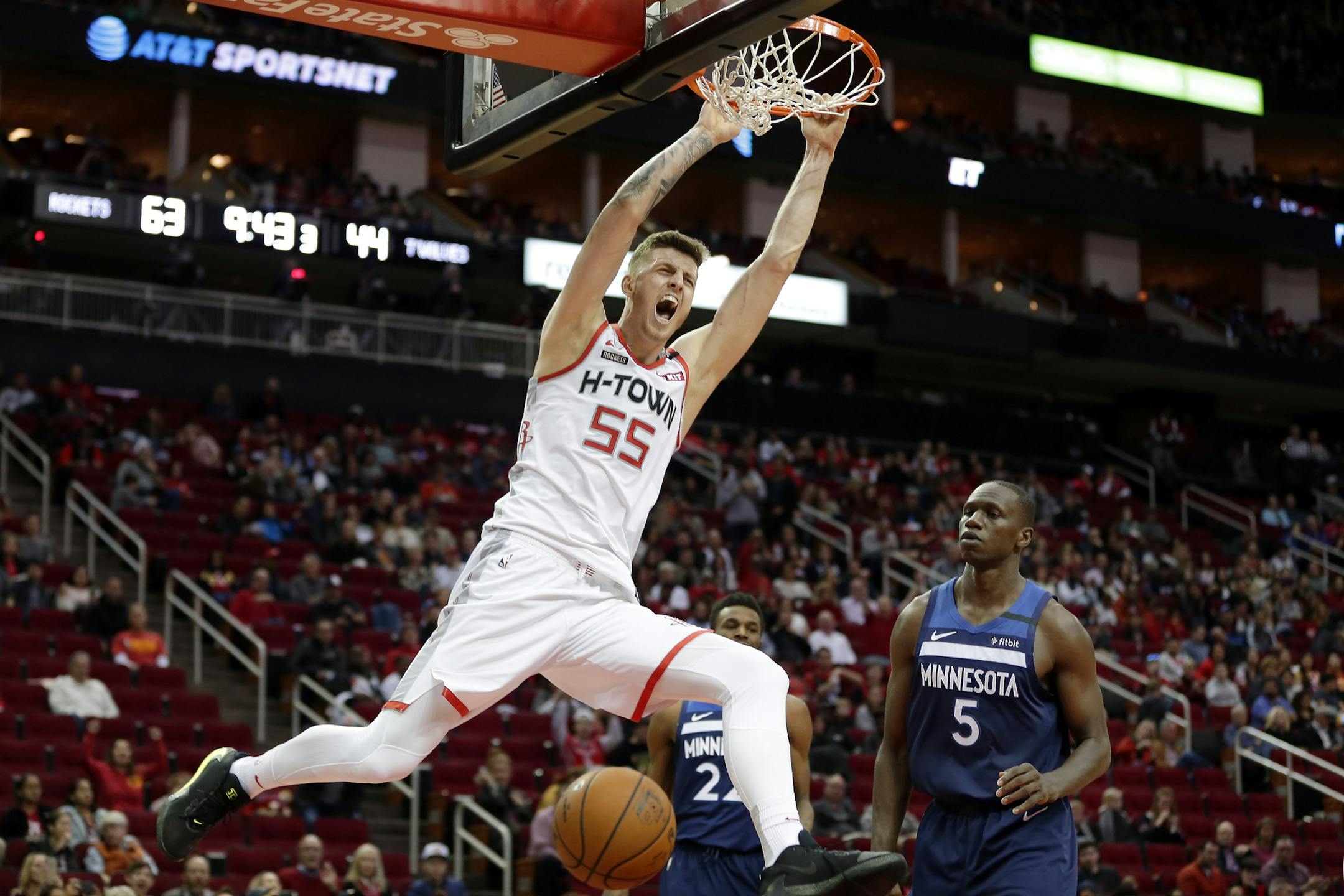 Houston Rockets center Isaiah Hartenstein (55) hangs from the rim after dunking as Minnesota Timberwolves center Gorgui Dieng (5) looks on during the second half of an NBA basketball game Saturday, Jan. 11, 2020, in Houston. (AP Photo/Michael Wyke)