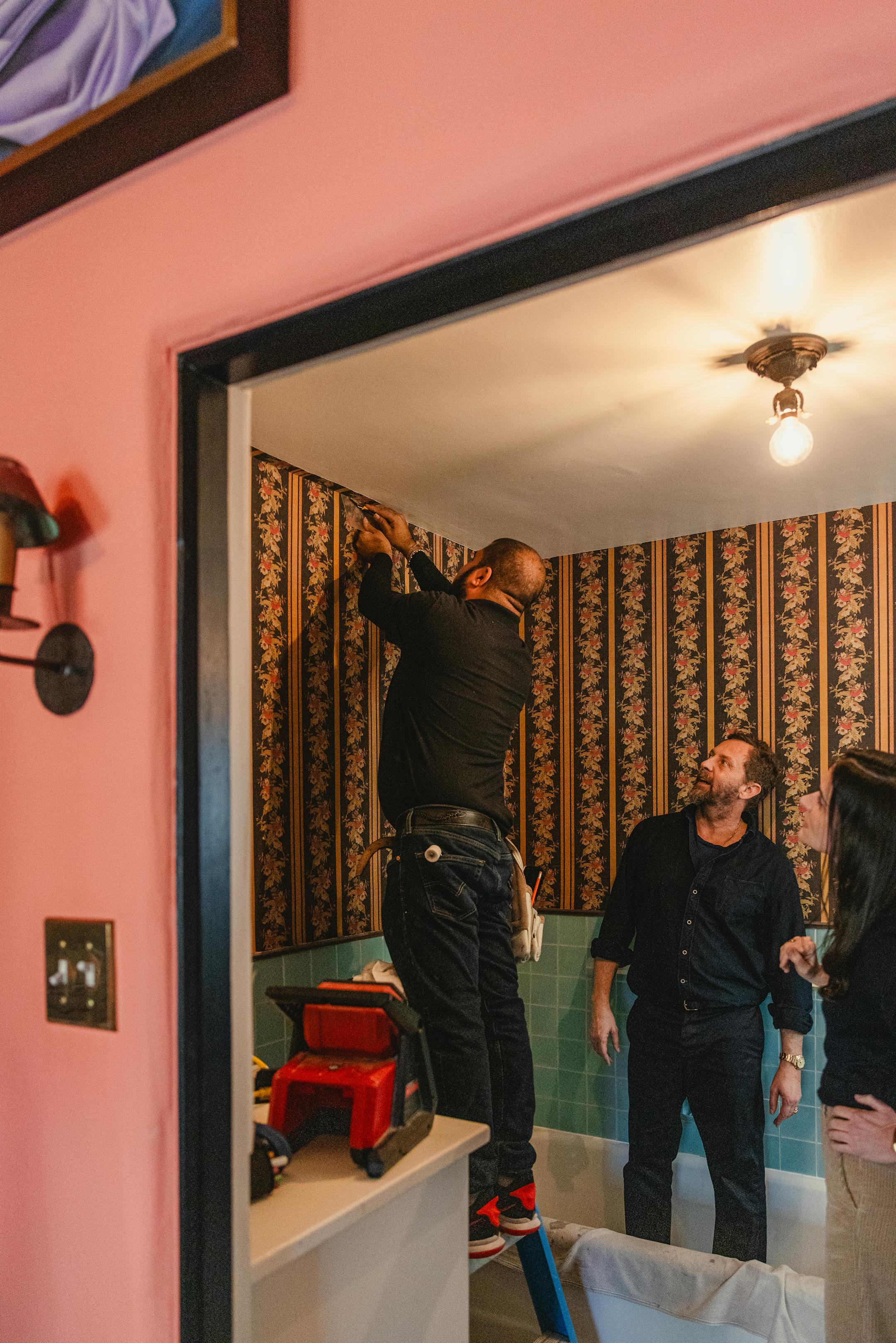 A worker installs a vertically striped wallpaper in a bathroom.