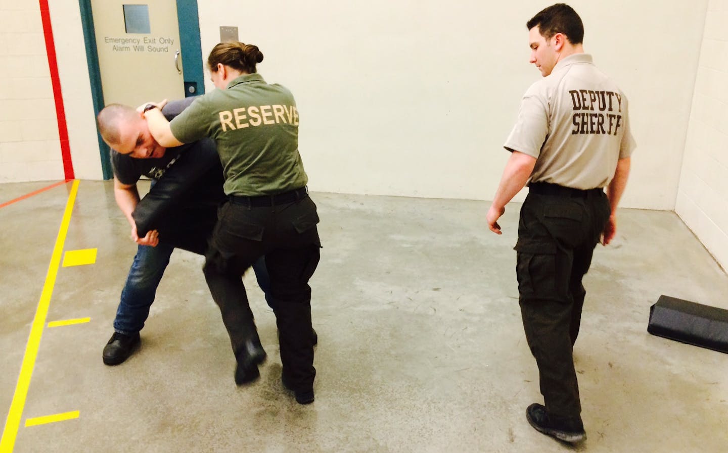 Deputy Justin Kaeding, a defensive tactics trainer for the Sheriff's Office, watches Dani Krinke's footwork as she practices a knee strike on recruit Brian Eich.