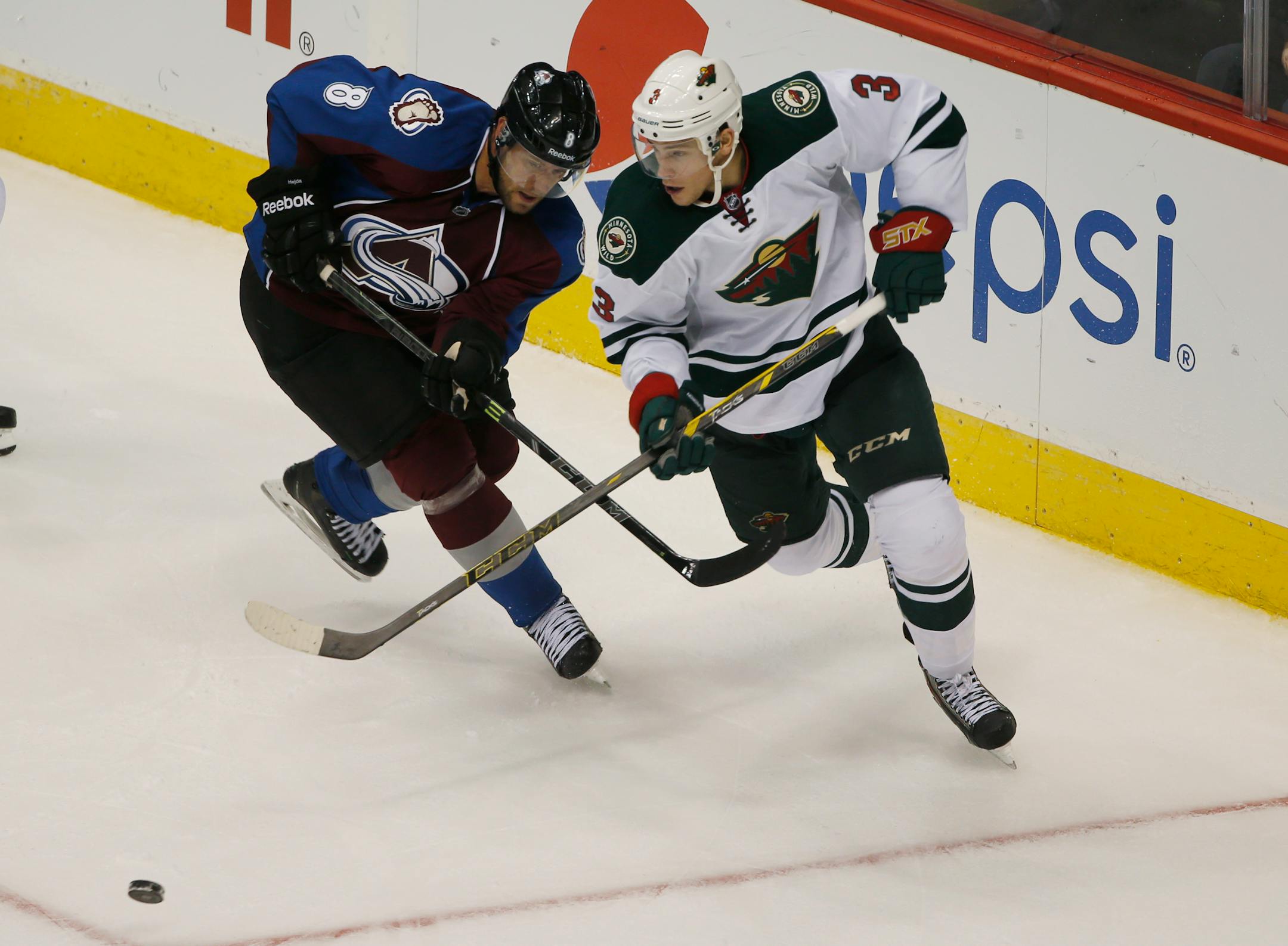 Minnesota Wild center Charlie Coyle, right, pursues puck with Colorado Avalanche defenseman Jan Hejda, of the Czech Republic, in the third period of the Wild's 3-0 victory in an NHL hockey game in Denver on Saturday, Oct. 11, 2014. (AP Photo/David Zalubowski)