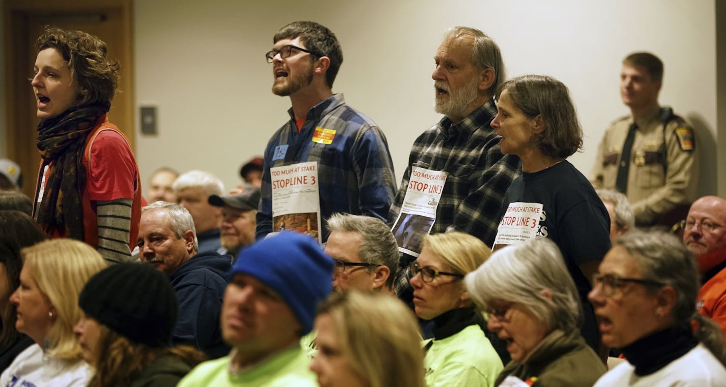 Paige Carlson, far left, and Andy Pearson, of MN350, a climate change environmental group, disrupt the ongoing discussions during a Public Utilities Commission meeting before leaving voluntarily Monday, Nov. 19, 2018, in St. Paul. Public Utilities Commission considers stipulations to its June approval for Enbridge's Line 3 pipeline. (Richard Tsong-Taatarii/Star Tribune via AP)