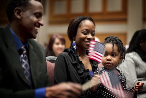 Mohamed Adam from Somalia made friends with Alfreanna Reeves, 2 as they waved flags to John Philip Sousa's Stars and Stripes Forever. Holding Alfreanna is her mom Alfrie Reeves. Approximately 1,300 immigrants from 99 different countries were sworn in as new U.S. citizens Thursday morning during a naturalization ceremony at the Minneapolis Convention Center, Thursday, January 24, 2013.