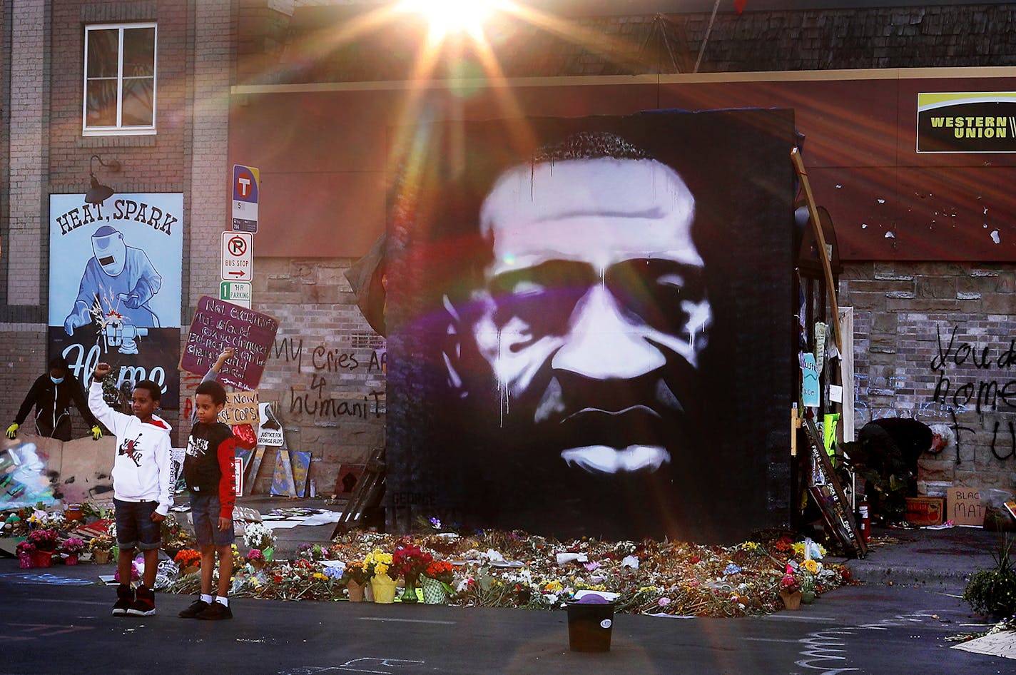 As the morning sun rose Brothers Josiah, 10, left to right, and Jay Russell, 8, posed for a photo by their father Joe Russell (not pictured) near a large George Floyd painting outside Cup Foods, where Floyd was killed in Minneapolis police custody and seen Friday, June 12, 2020, in Minneapolis, MN.] DAVID JOLES • david.joles@startribune.com Young brothers pose near George Floyd painting outside Cup Foods, where Floyd was killed in Minneapolis police custody and the site of a large Memorial to Fl