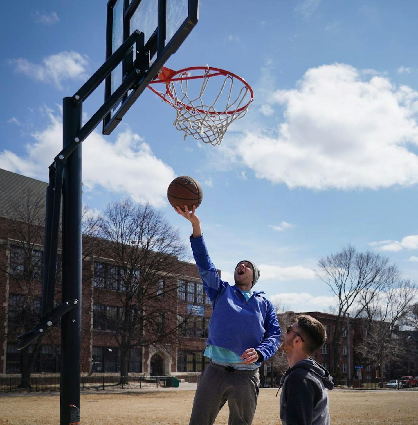 A group of recent Macalester grads meet frequently to play basketball. Since their gym is closed, but mostly because the weather is warming up, they met on the outdoor court at Jefferson Community School in Minneapolis to shoot around and be in the sun. In this photo, Isaac Siegel shot a layup while Mac Doherty waited for a rebound.