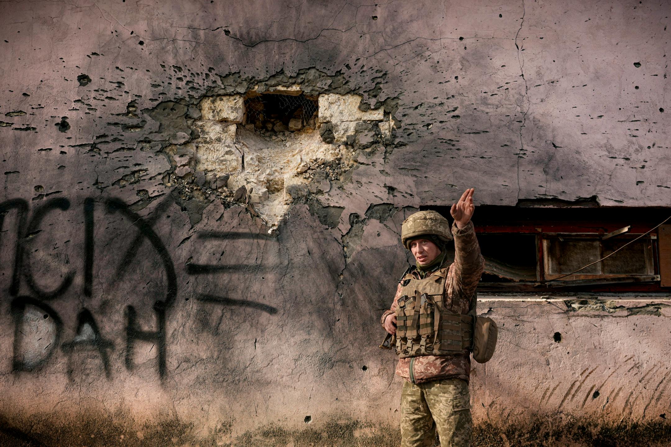 A Ukrainian serviceman points to the direction of the incoming shelling next to a building which was hit by a large caliber mortar shell in the frontline village of Krymske, Luhansk region, in eastern Ukraine, Saturday, Feb. 19, 2022. Ukrainian President Volodymyr Zelenskyy, facing a sharp spike in violence in and around territory held by Russia-backed rebels and increasingly dire warnings that Russia plans to invade, on Saturday called for Russian President Vladimir Putin to meet him and seek resolution to the crisis. (AP Photo/Vadim Ghirda)