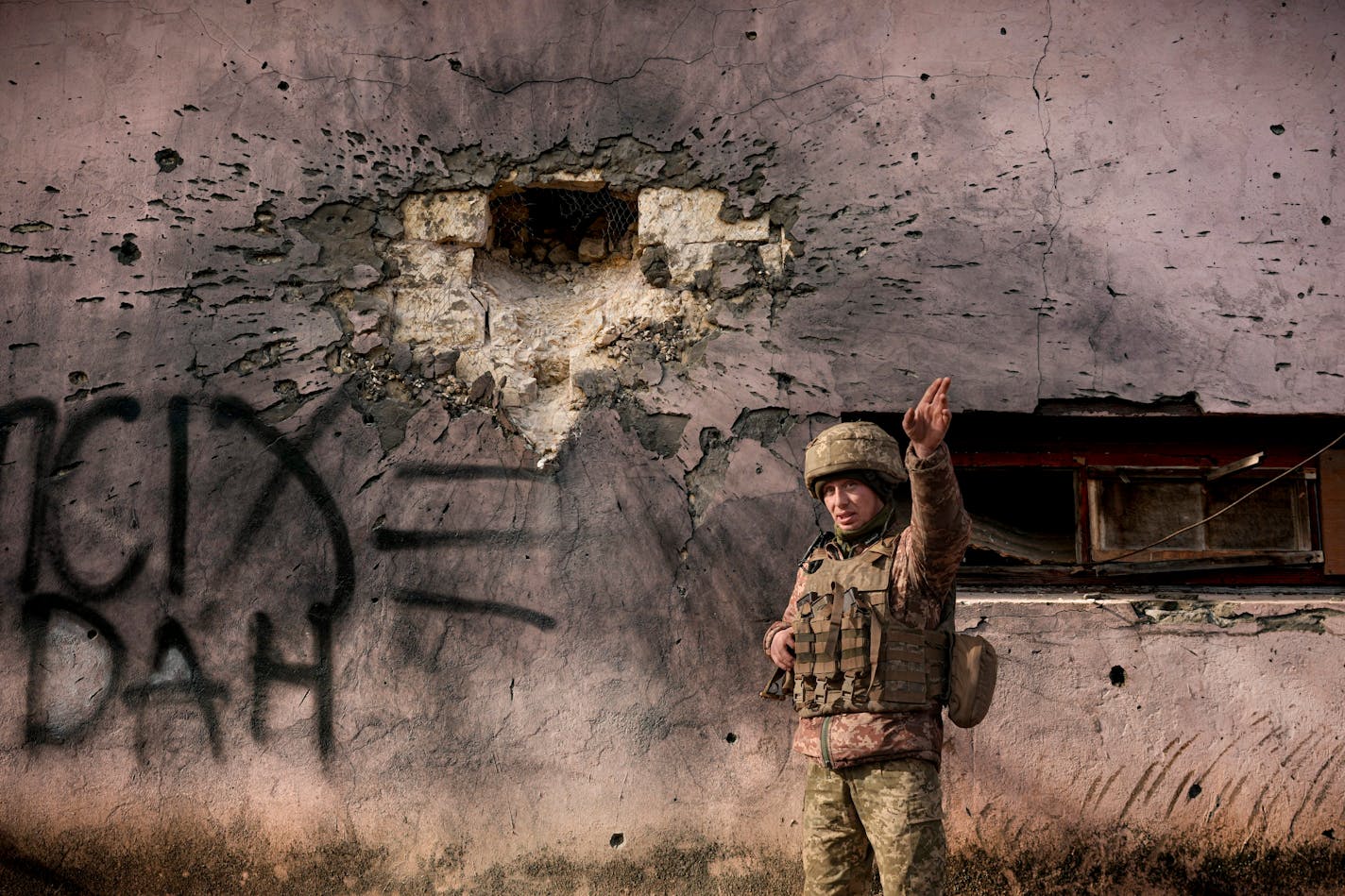 A Ukrainian serviceman points to the direction of the incoming shelling next to a building which was hit by a large caliber mortar shell in the frontline village of Krymske, Luhansk region, in eastern Ukraine, Saturday, Feb. 19, 2022. Ukrainian President Volodymyr Zelenskyy, facing a sharp spike in violence in and around territory held by Russia-backed rebels and increasingly dire warnings that Russia plans to invade, on Saturday called for Russian President Vladimir Putin to meet him and seek resolution to the crisis. (AP Photo/Vadim Ghirda)