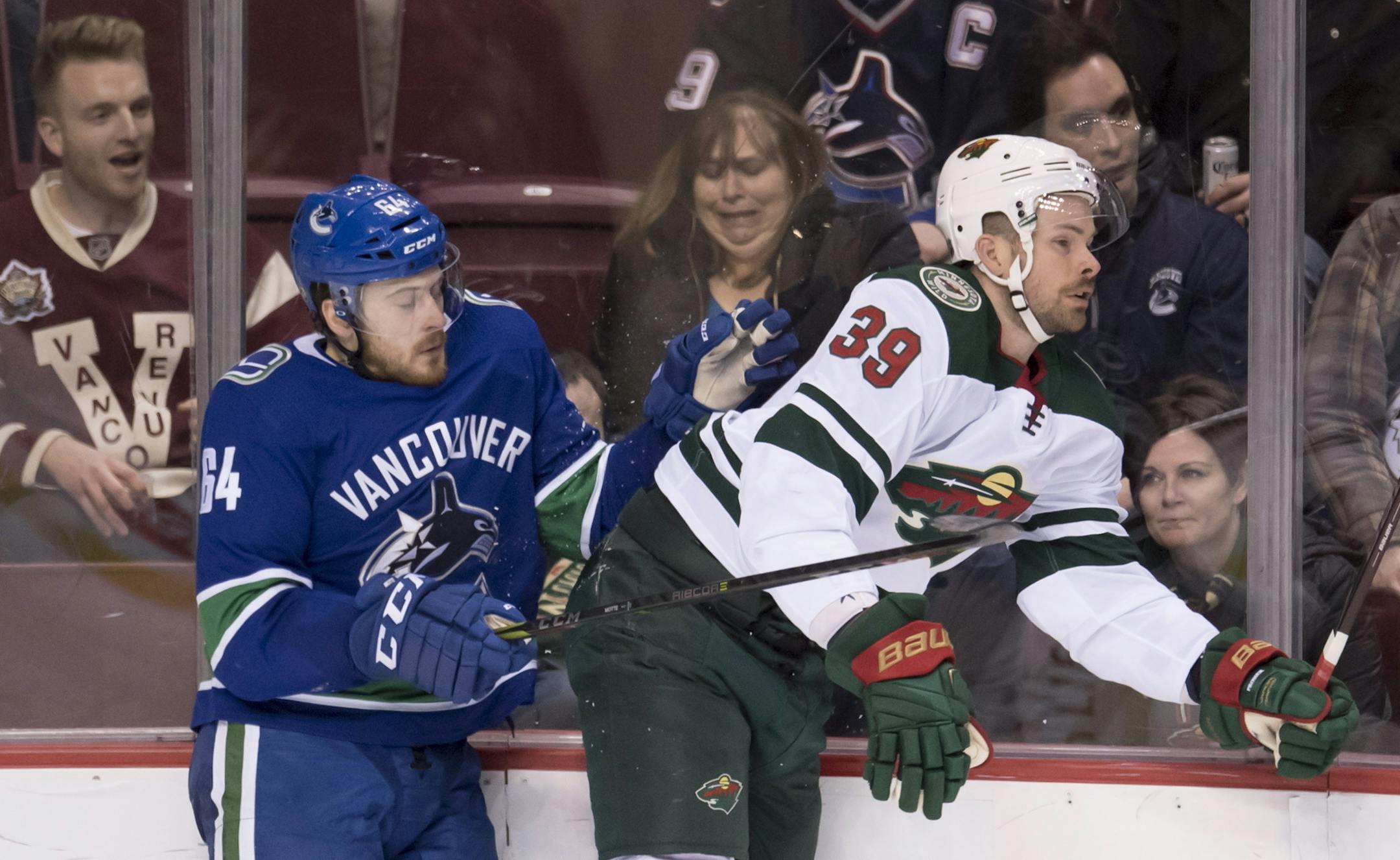 Vancouver Canucks center Tyler Motte (64) goes into the boards with Minnesota Wild defenseman Nate Prosser (39) during the first period of an NHL hockey game Friday, March 9, 2018, in Vancouver, British Columbia. (Jonathan Hayward/The Canadian Press via AP)