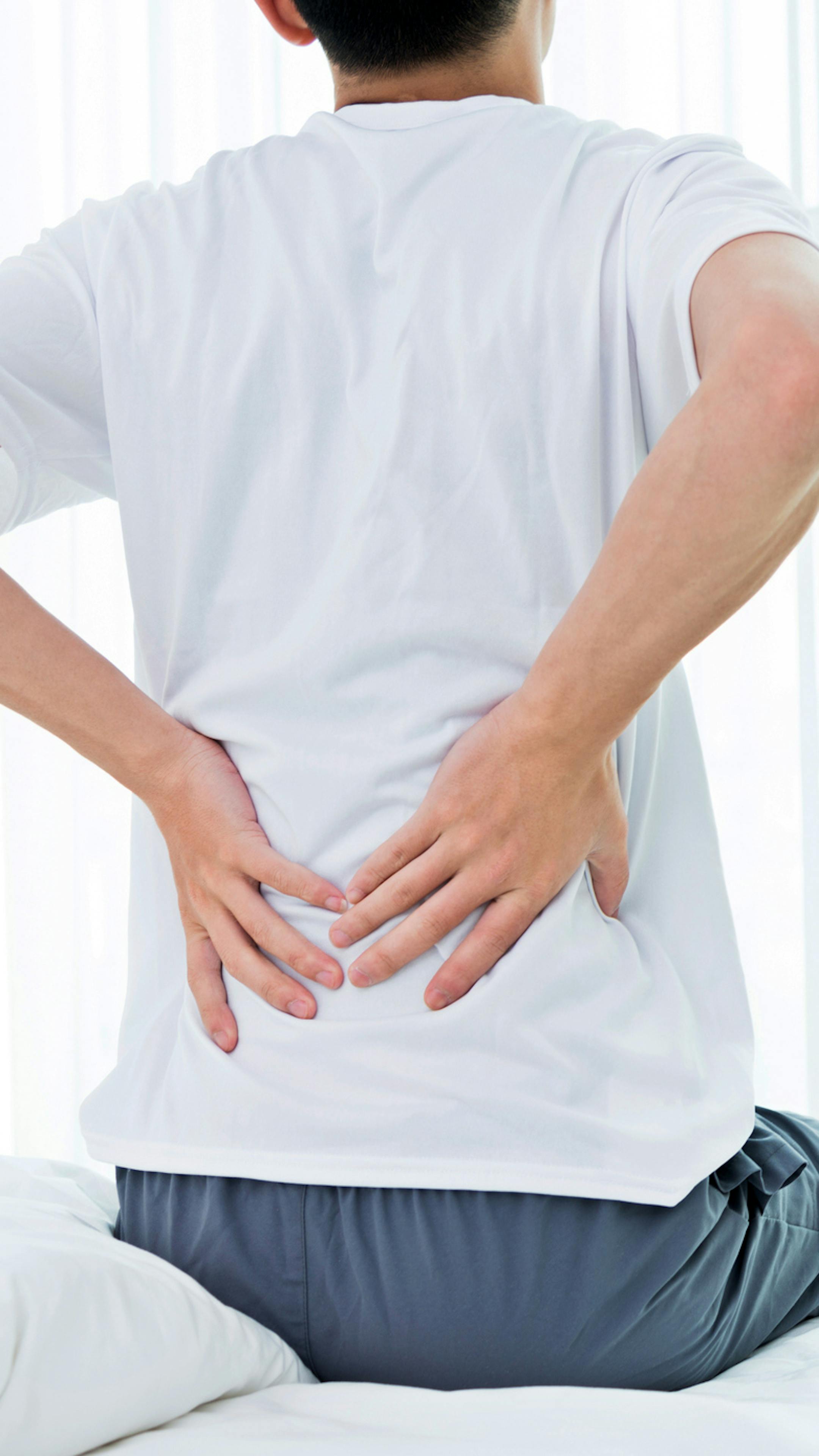 Young man sitting on the bed suffering from backpain.