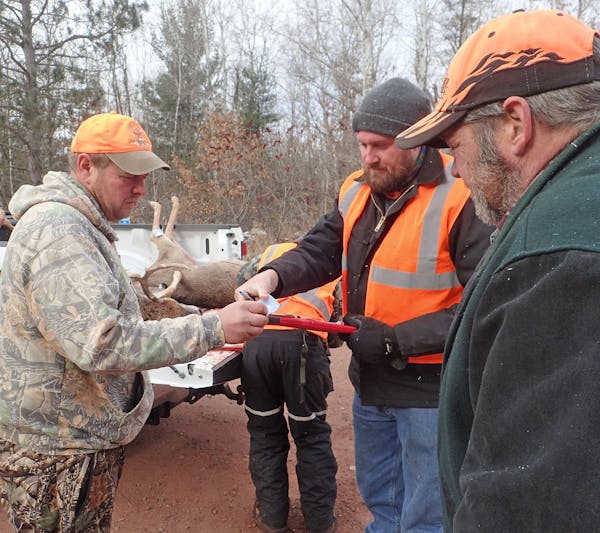 Brian Beck of Princeton, left, goes over paperwork with DNR biologist Andy Tri (holding clipboard) while checking in two deer at the CWD sampling stat
