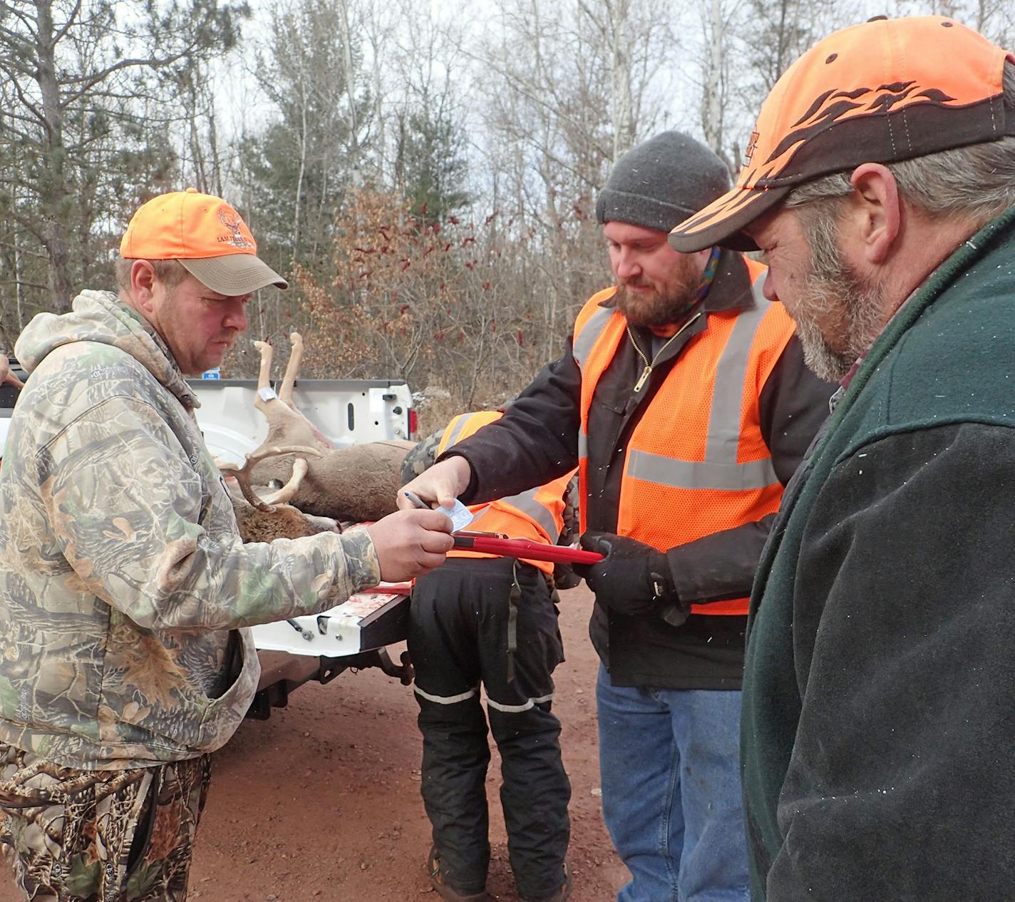 Brian Beck of Princeton, left, goes over paperwork with DNR biologist Andy Tri (holding clipboard) while checking in two deer at the CWD sampling station in Crosby, Minn., last week.