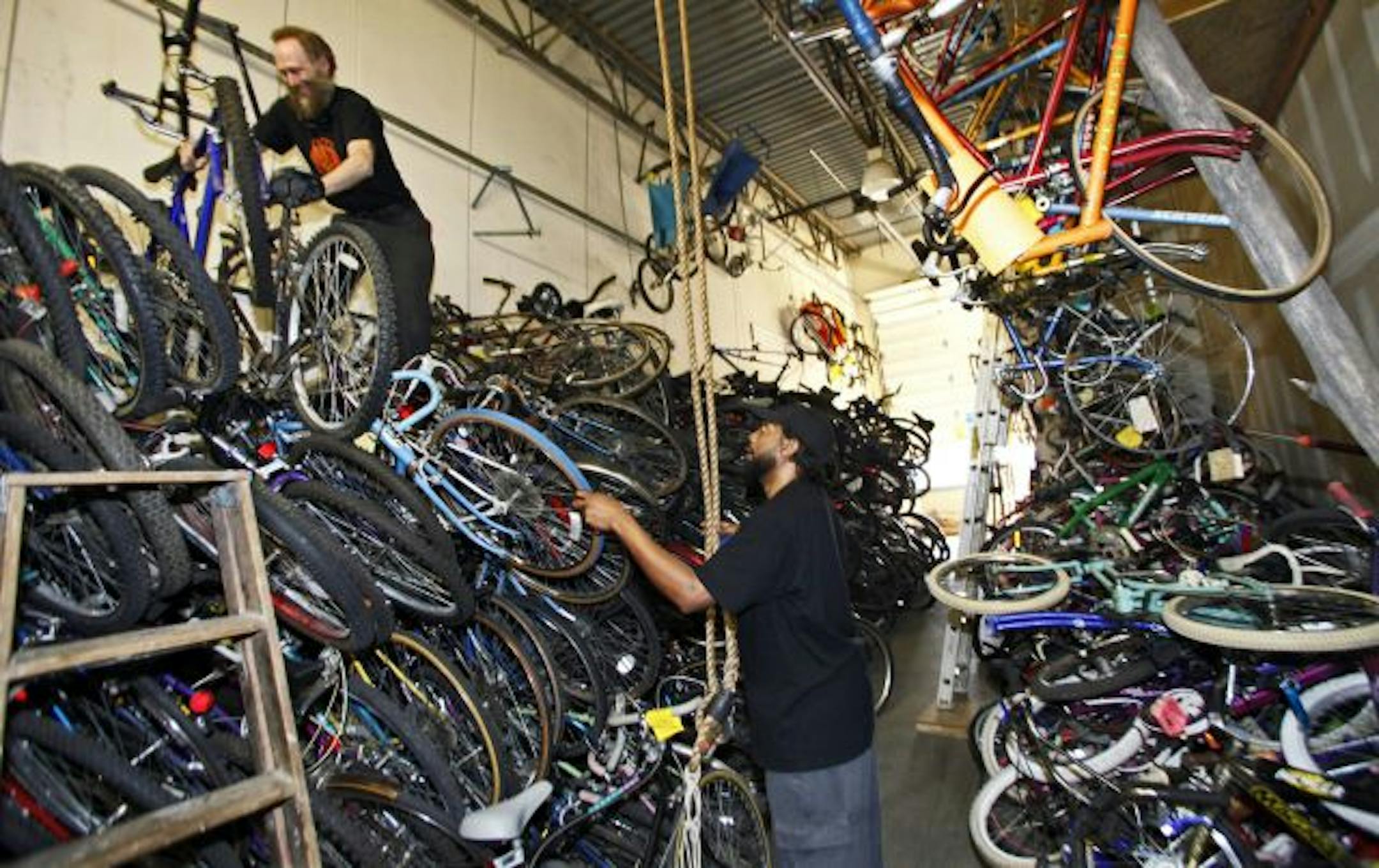 The is the raw material of which bike dreams are made. John Finkle, left, who is on the bike library's board of directors, pulled down a bike from a stack of 250 for volunteer Nathaniel Dowls, who will put the bike back into road-worthy shape.
