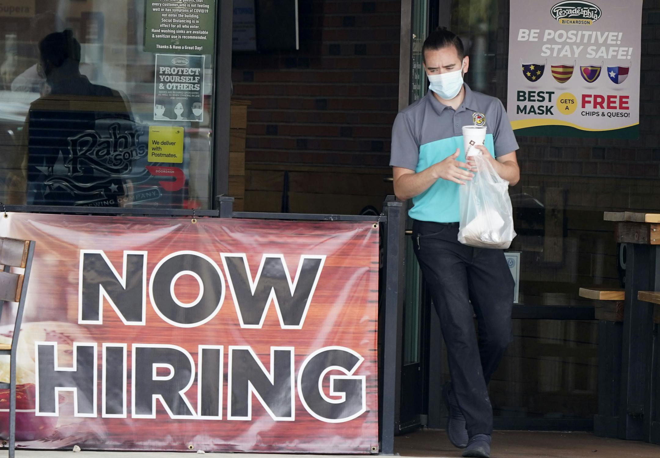 In this Sept. 2, 2020 file photo, a customer wore a face mask as they carry their order past a now hiring sign at an eatery in Richardson, Texas. On Thursday, Nov. 5, the number of Americans seeking unemployment benefits fell slightly last week to 751,000, a still-historically high level that shows that many employers keep cutting jobs in the face of the accelerating pandemic.