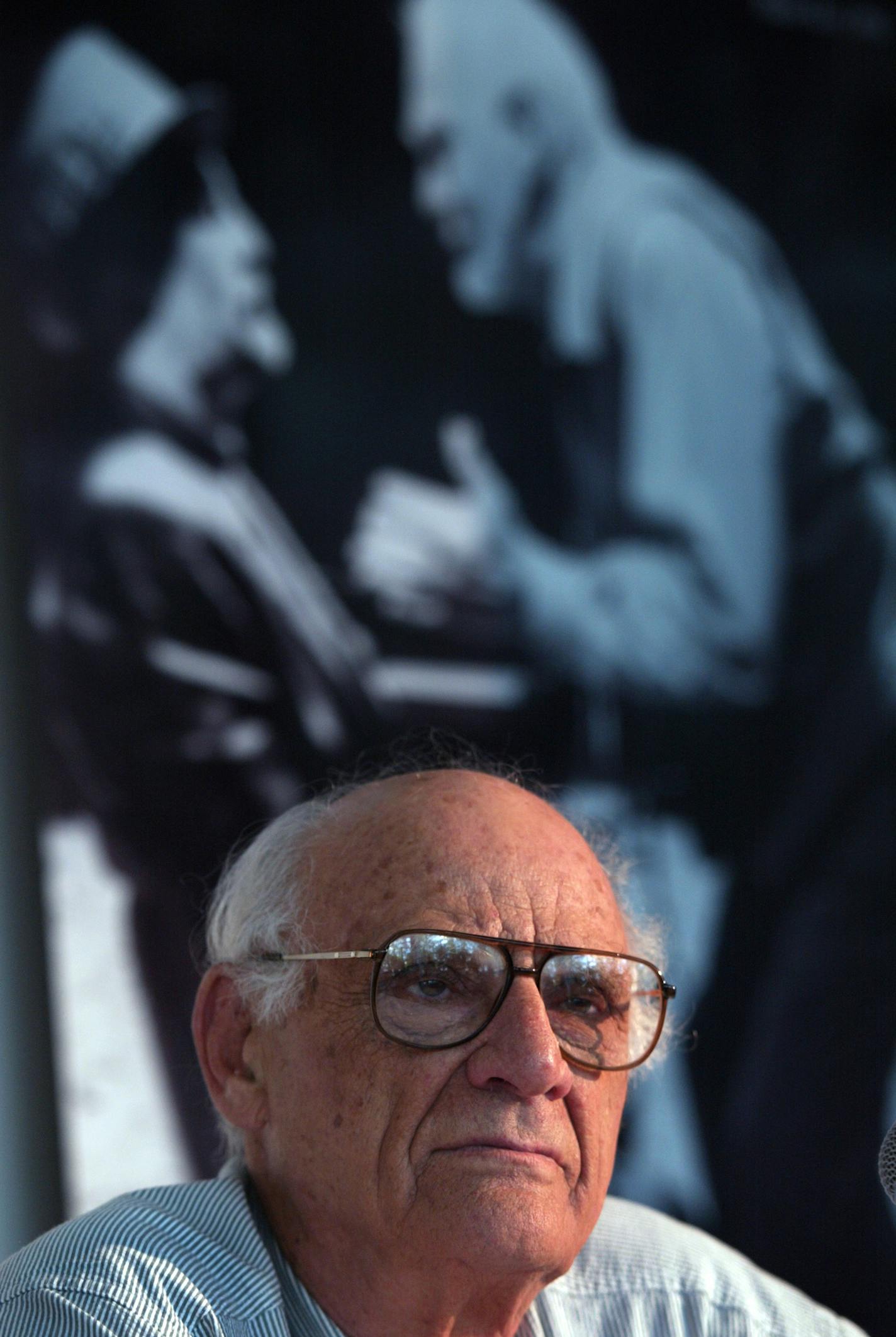 GENERAL INFORMATION: 7/3/02- Minneapolis, MN - Playwright Arthur Miller at a press conference at the Guthrie Theater in Minneapolis discussing his upcoming play "Resurrection Blues" which will have its world premiere at the Guthrie. IN THIS PHOTO: With a lifesize photo of a scene from the play "Death of A Salesman" on the wall behind him, playwright Arthur Miller, in Minneapolis to work at the Guthrie Theater where his new play "Resurrection Blues" will have its world premiere, listens to a ques