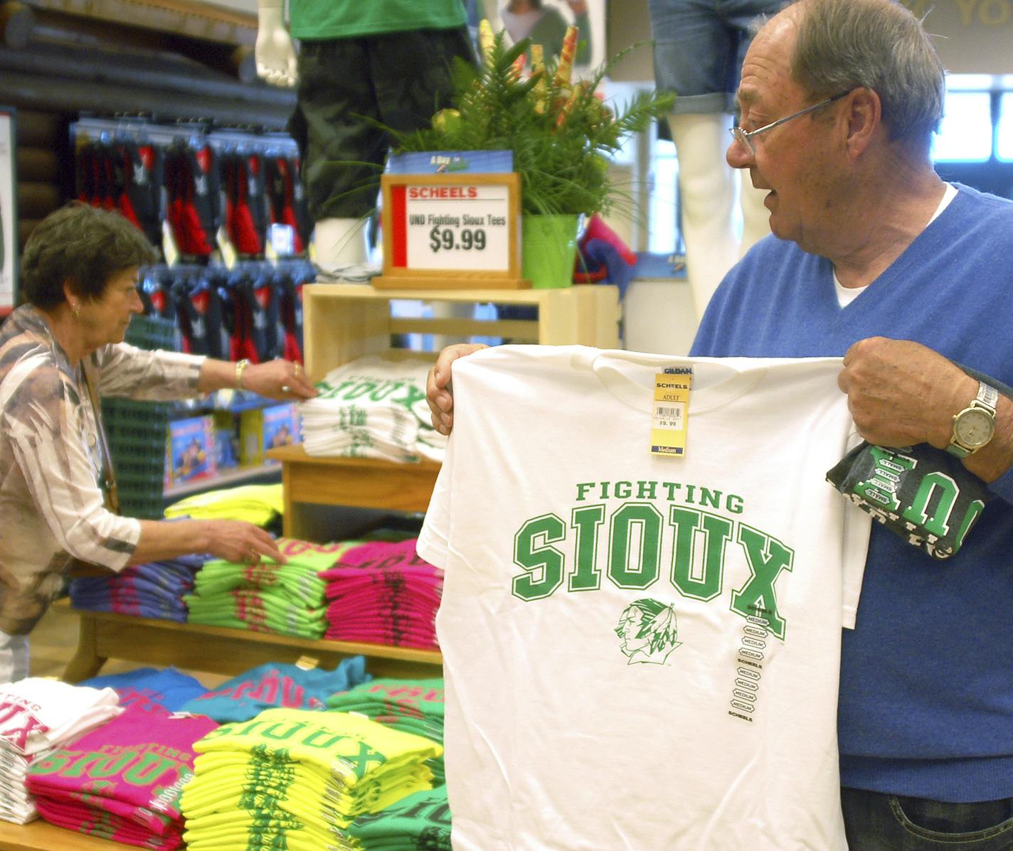 FILE - In this, Tuesday, June 12, 2012, file photo, Buck Striebel holds up a University of North Dakota Fighting Sioux T-shirt while his wife, GaeLynn, sorts through other shirts on sale at a sporting goods store in Bismarck, N.D. The school adopted the nickname the Fighting Hawks on Wednesday, Nov. 18, 2015, to replace the Fighting Sioux. Students across the United States are pressuring their colleges to update mascots, mottos and building names that they say are insensitive. (AP Photo/James Ma