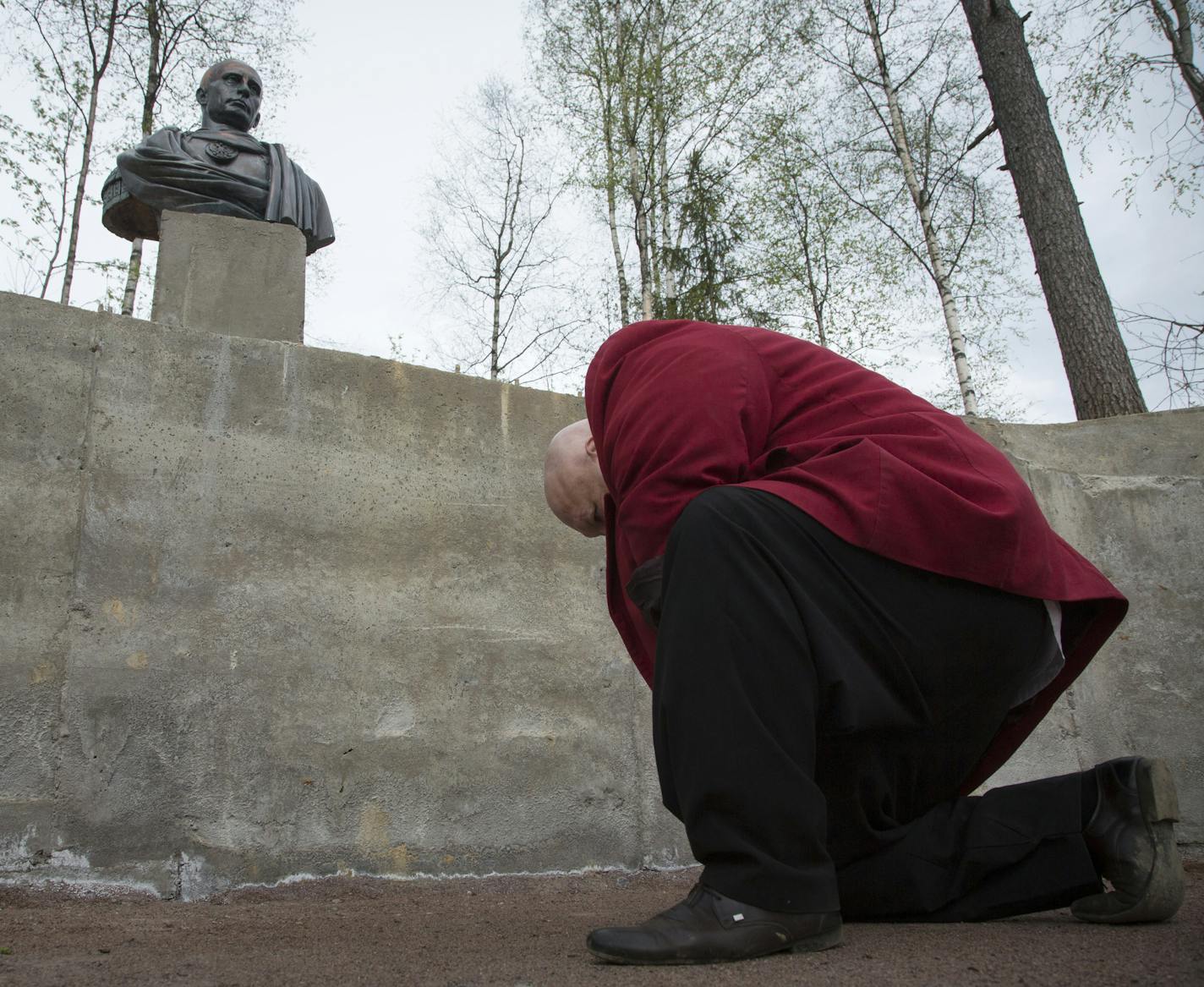 A man bows to a bust of Russian president Vladimir Putin in Kasimovo village, 30 km to the north of St.Petersburg, Russia, Saturday, May 16, 2015. The bust made of some synthetic material that looked like bronze featured Putin in an image of a Roman emperor dressed in toga. The bust was opened on a private fenced territory that belongs to the Cossacks. (AP Photo/Dmitry Lovetsky)