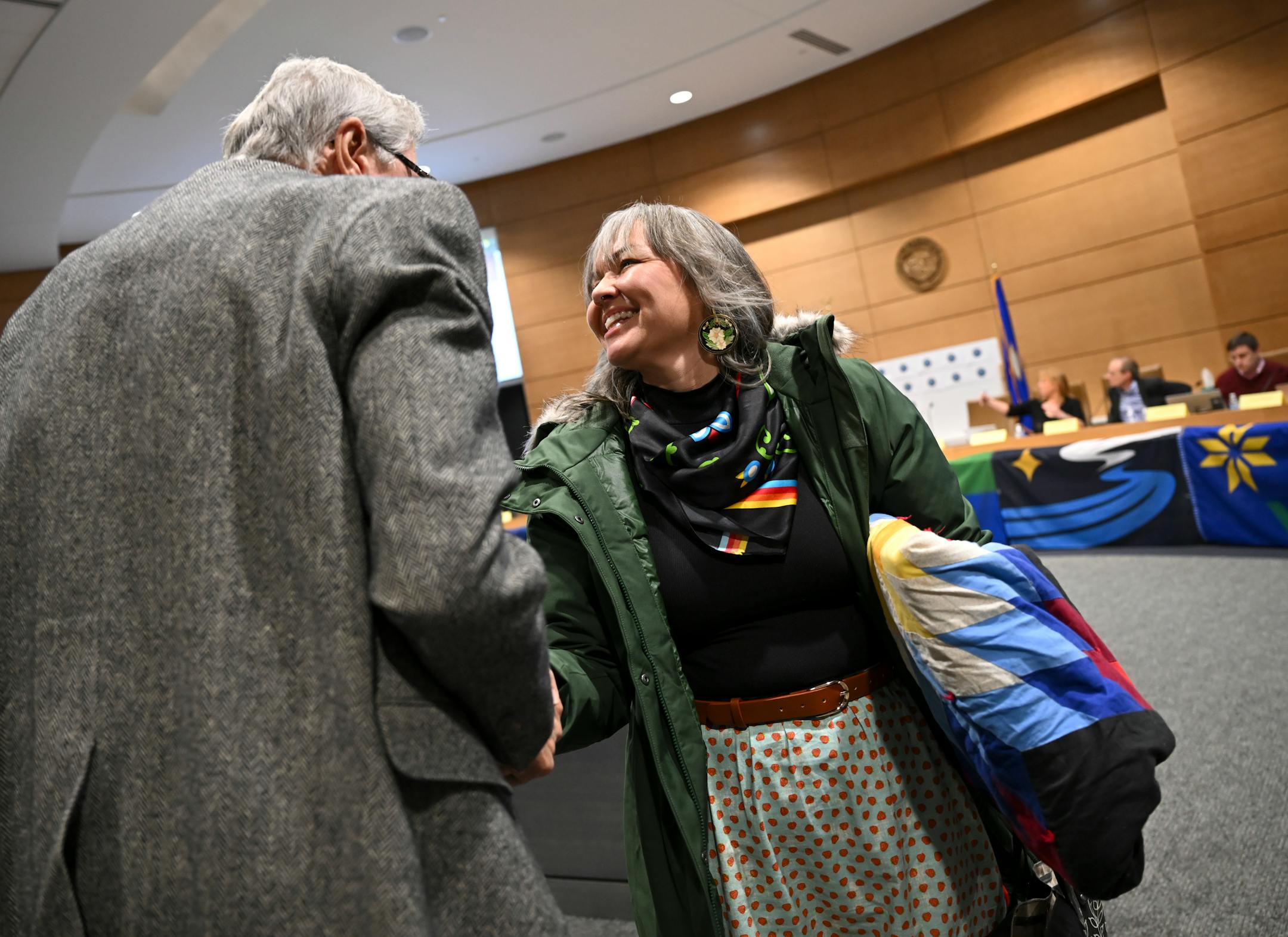 Sarah Agaton Howes and John Muller, both artists whose flags are finalists under consideration by the State Emblems Redesign Commission, greet each other during a recess Tuesday, Dec. 12, 2023 at the Minnesota Senate Building in St. Paul, Minn.. ] AARON LAVINSKY • aaron.lavinsky@startribune.com