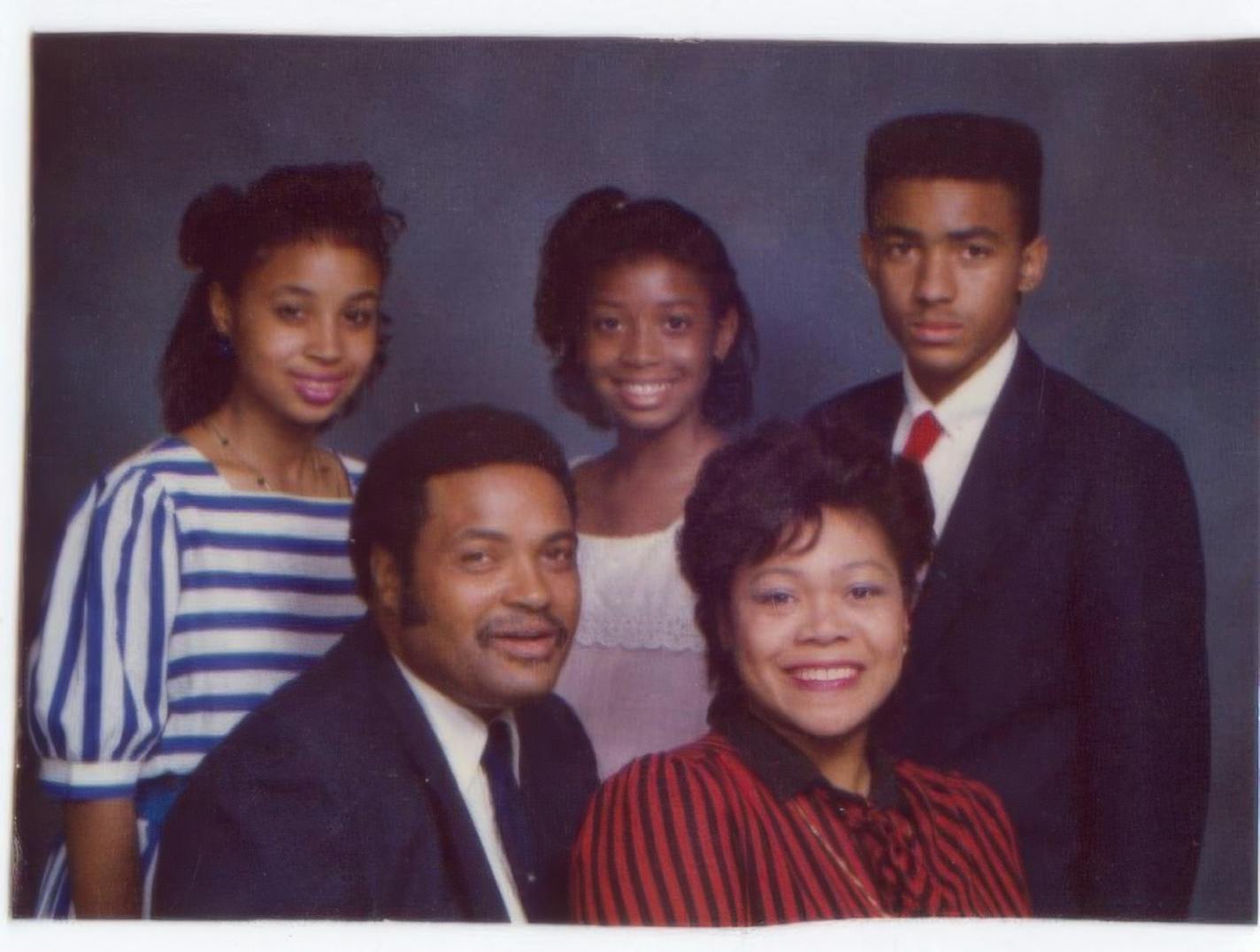 A family portrait of two parents in suit and dress seated in front of two adolescent girls and a boy