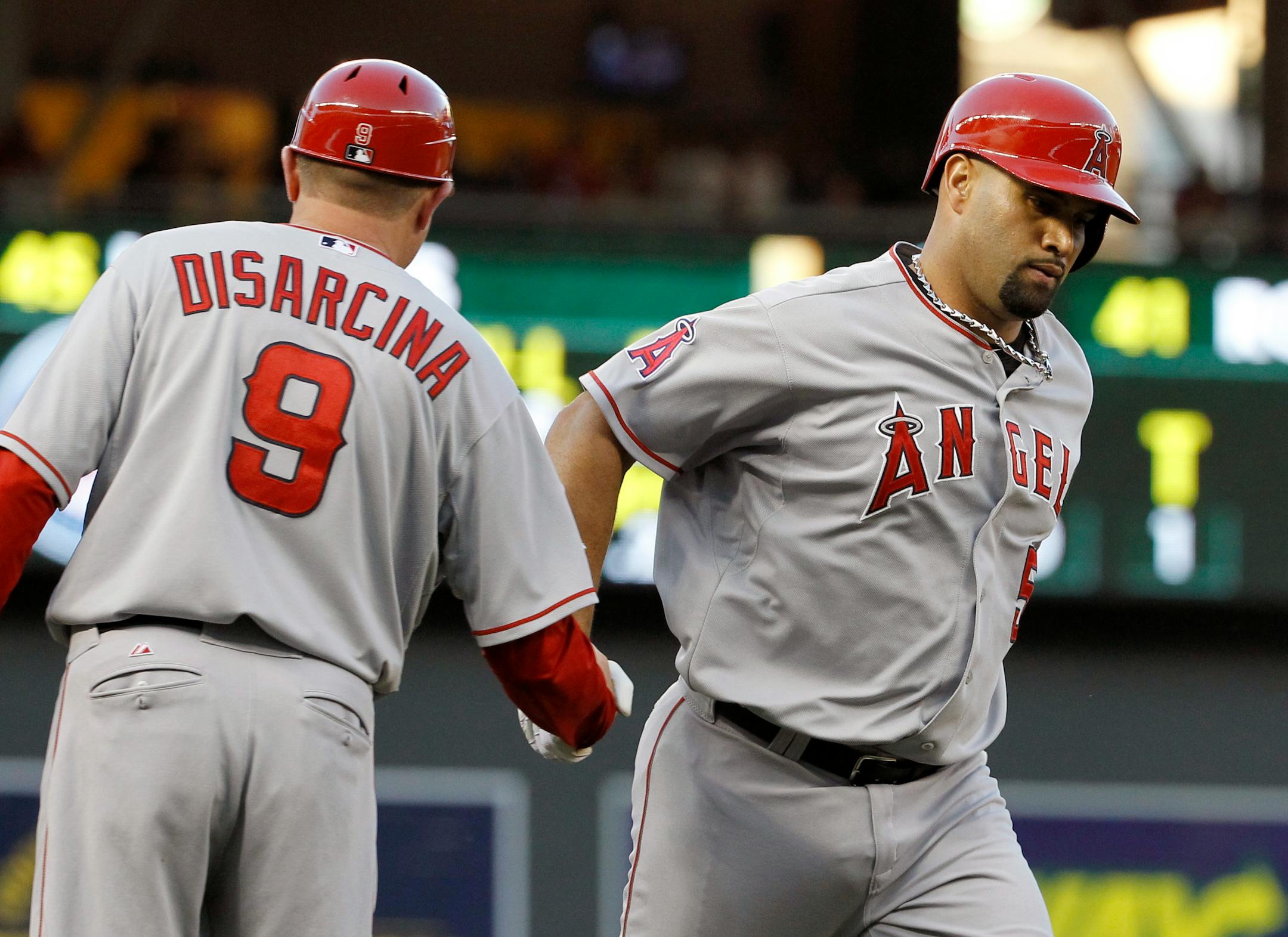 Los Angeles Angels third base coach Gary DiSarcina (9) congratulates Albert Pujols, right, who rounds third on a solo home run off Minnesota Twins pitcher Phil Hughes during the third inning of a baseball game in Minneapolis, Saturday, Sept. 6, 2014. (AP Photo/Ann Heisenfelt)