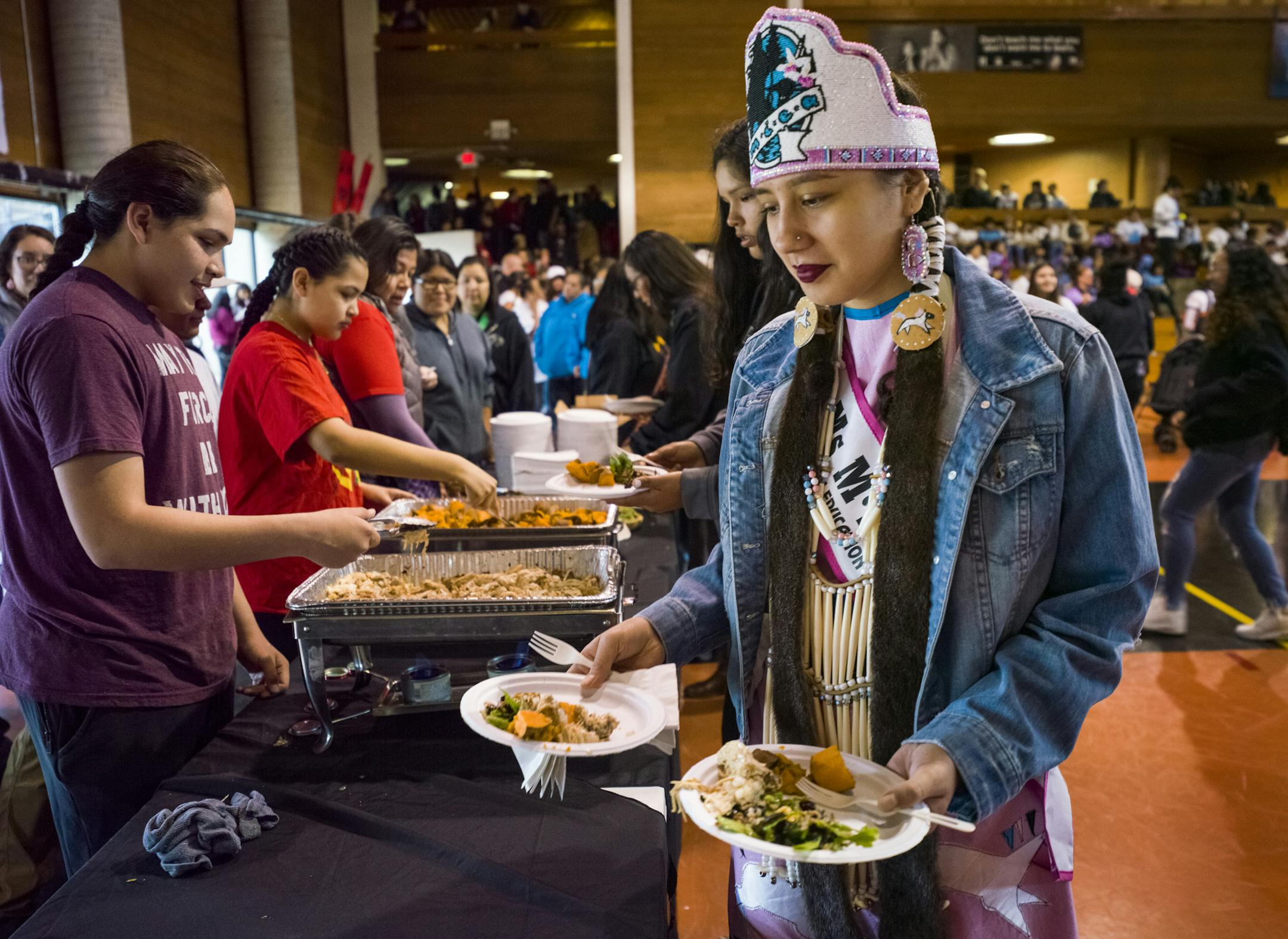 Miiskogihmiiwan Poupart-Chapman, Ms. M.I.E.A.( Minnesota Indian Education Association) for 2018-19 got in line to get food to serve elders. The community feast was prepared by Brian Yazzie, a Native American chef who incorporated wild rice from White Earth, and organic ingredients in the feast of turkey and salad. "Food sovereignty is being able to sustain yourself," said the 18-year old from Lac Du Flambeau, Wisconsin who has volunteered with Dream of Wild Health.] Community feast at Minneapoli