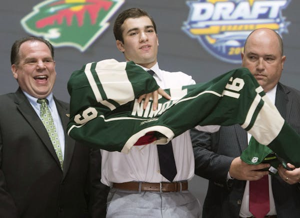 Luke Kunin, second from right, puts on his sweater as he stands with members of the Minnesota Wild management team at the NHL draft in Buffalo, N.Y., 