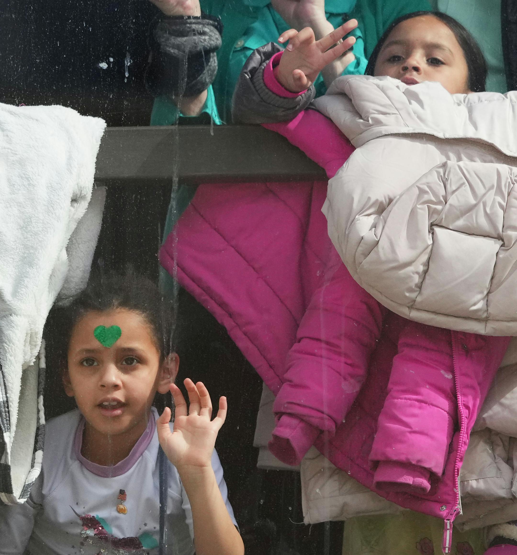 Children in a skyway wave to participants in the St. Paul's St. Patrick's Day parade below them.