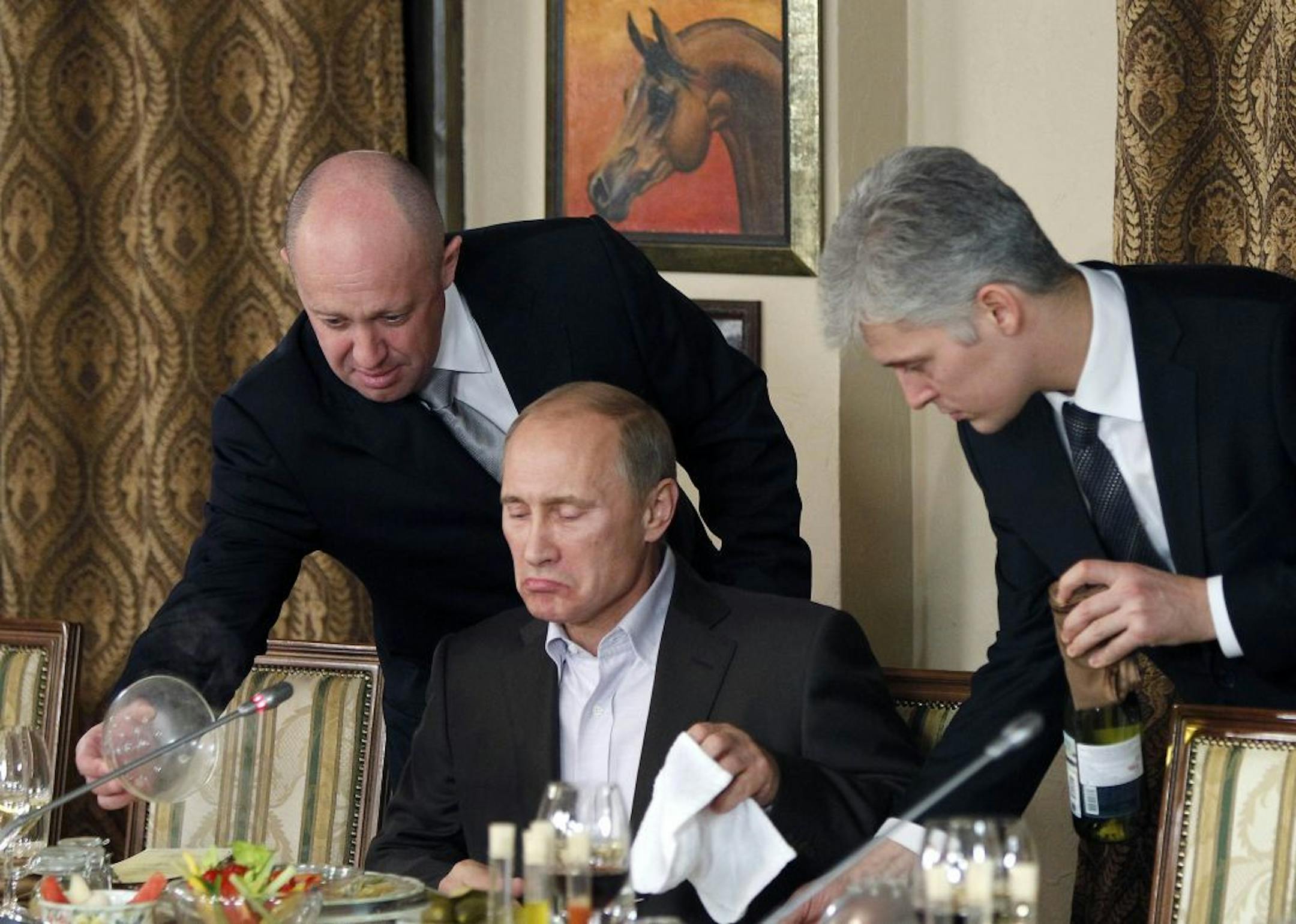 FILE - In this Friday, Nov. 11, 2011 file photo, businessman Yevgeny Prigozhin, left, serves food to Russian Prime Minister Vladimir Putin, center, during dinner at Prigozhin's restaurant outside Moscow, Russia. Ten years ago, he served plates to President Vladimir Putin. These days, St. Petersburg-based businessman Yevgeny Prigozhin funds Kremlin trolls and sends mercenaries to help Russia's military operation in Syria _ all with one aim: to do the president favors that would be too risky for o