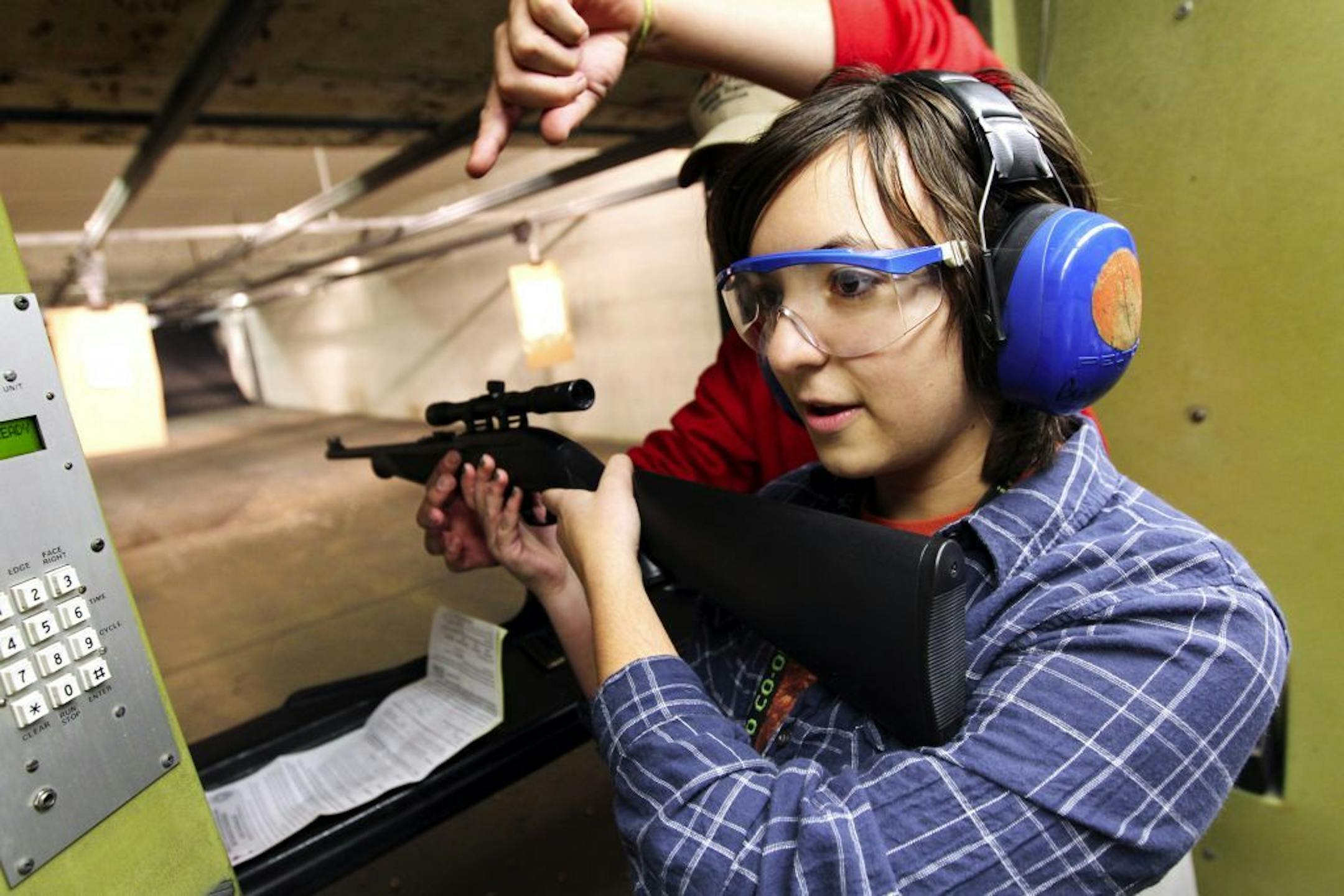 Instructor Jason Raaen, back, prepares Liz Davey, 19, to shoot a rifle for the first time at Burnsville Rifle and Pistol Range October 15, 2011. Davey completed a Personal Firearms Safety Training course and will go on an inaugural deer hunt this year. She had approached Tim Magdik, her mother's boyfriend, for help in securing her license and learning how to hunt. Magdik joined Davey at the gun range and is honored that she's seeking his wisdom. "If she gets a deer," says Magdik, "I'll be passin