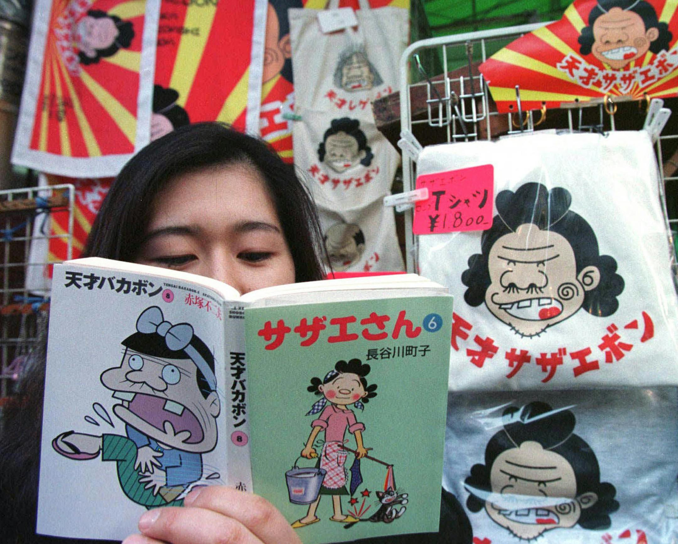 ** FILE ** A woman poses with a cartoon book with a cover made from two popular cartoons, Bakabon, left, a mangy gardener, and Sazae-san, right, the demure housewife, beside a T-shirt featuring "Sazaebon," a mutant character of the two at an open air stall in downtown Tokyo in this Thursday, March 6, 1997 file photo. Japan will hand out its first "Nobel Prize of Manga" this summer for artists in the comic book genre abroad, the Foreign Ministry said Tuesday, May 22, 2007, _ another step in its e