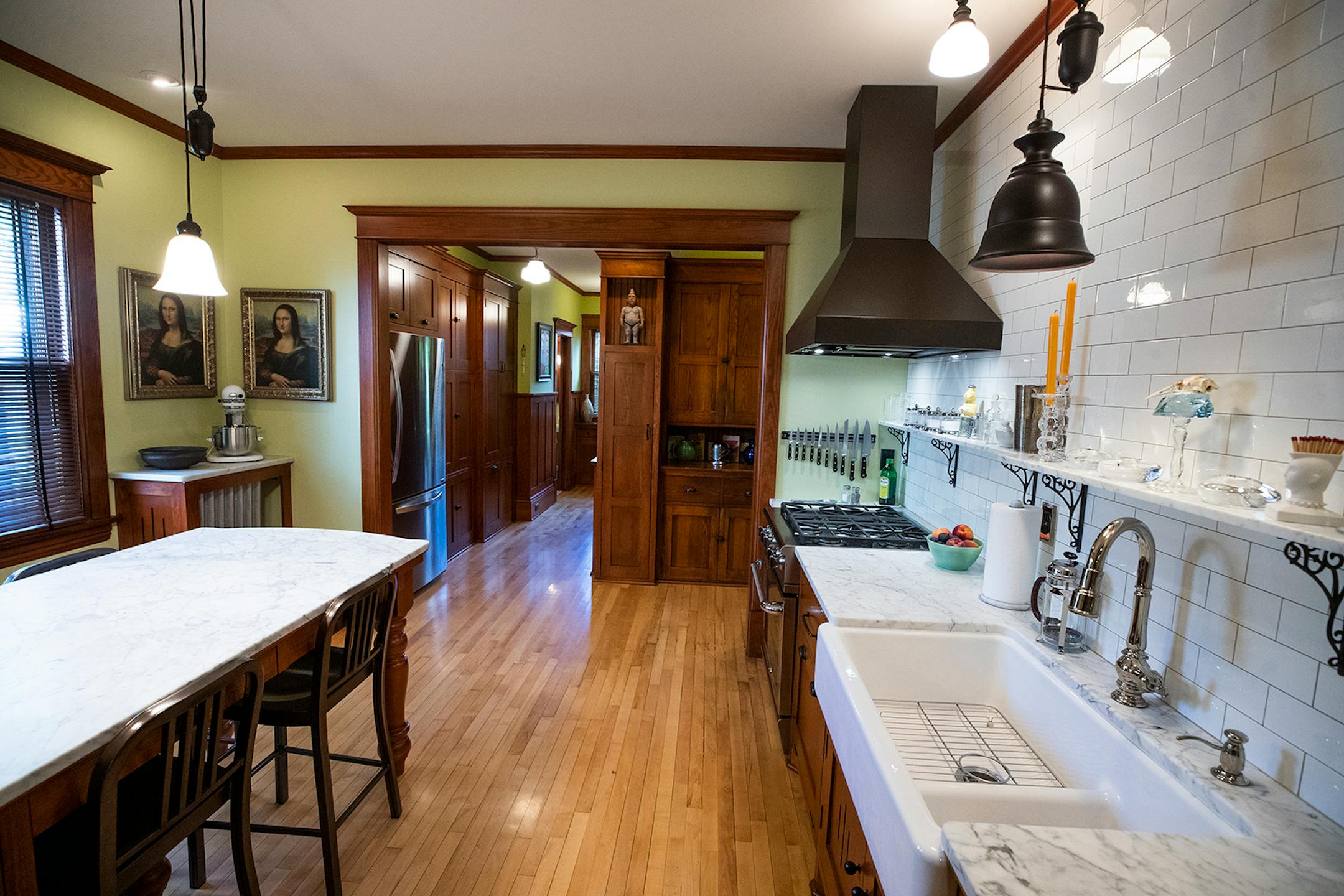 The remodeled kitchen features Carrara marble countertops, a built-in table, also topped with Carrara marble, a farm sink and period-looking light fixtures.