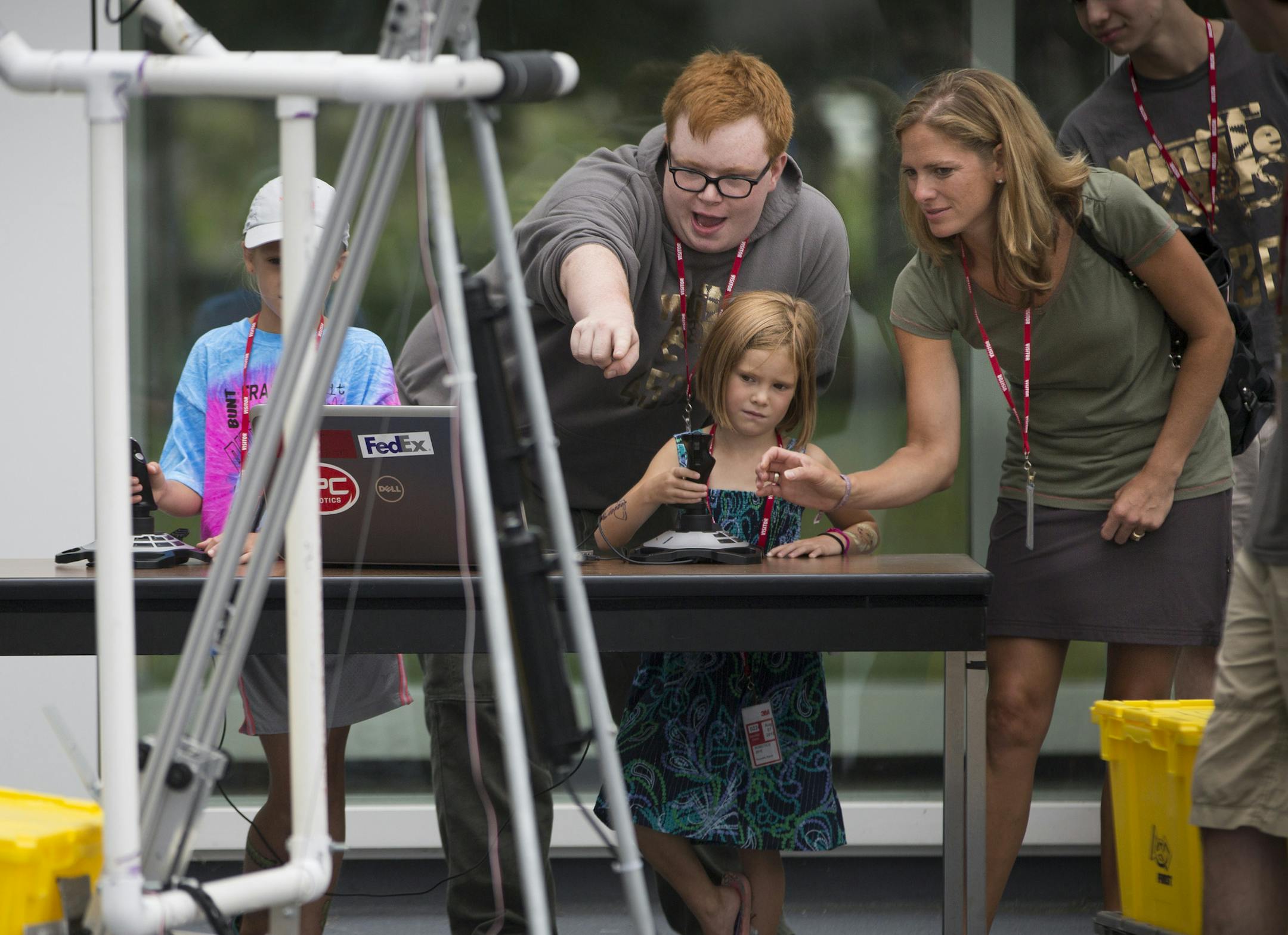Henry O'Callaghan pointed to a robot he and his Central High School robotics teammates created as he let five-year-old Natalie Loewe and her mom Allyson Loewe drive using a joystick during an event that had local high school students from the 14 area school's 3M sponsors in Robotics showing off incredible robots they made themselves at the 3M plaza on Thursday, August 7, 2015 in Woodbury, Minn. ] RENEE JONES SCHNEIDER &#x2022; reneejones@startribune.com