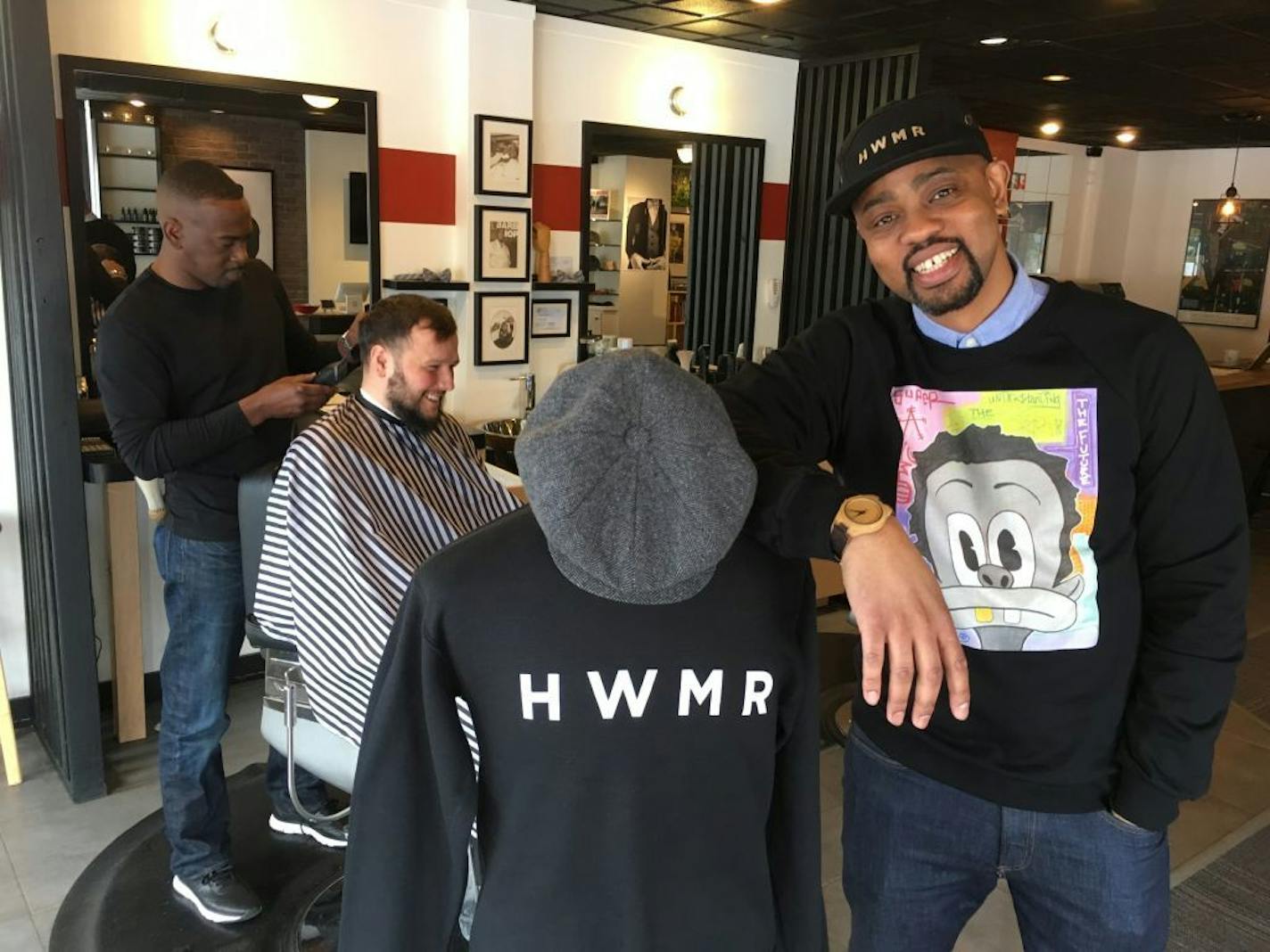 Houston White, right, modeled some of his clothing at his refurbished headquarters in the Camden neighborhood of north Minneapolis. At left, barber Shone Scott cut the hair of customer Jon Crappel.