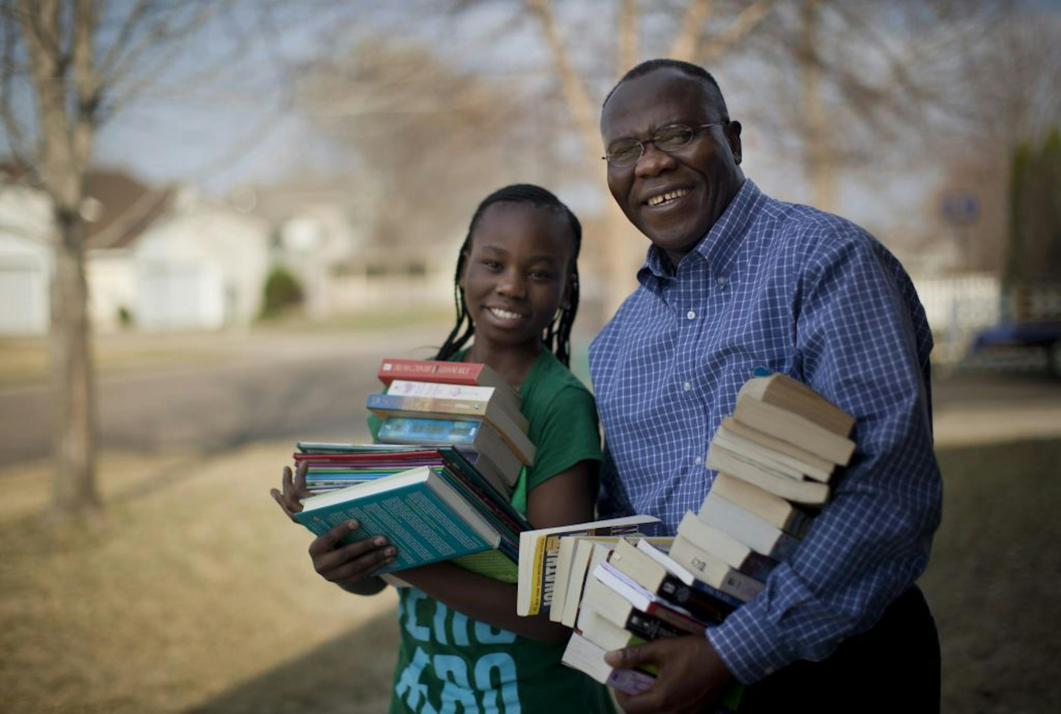 Atare Agbamu and his daughter Tejiri Agbamu posed on Monday, March 19, 2012 in Oakdale, Minn., with stacks of books they've collected to send to Atare's homeland Nigeria where he discovered an empty library in the local school while visiting recently. This Oakdale man and his family have gathered thousands of books into three big shipments and continue to buy more from thrift shops and collect to send abroad to help the young Nigerians learn.