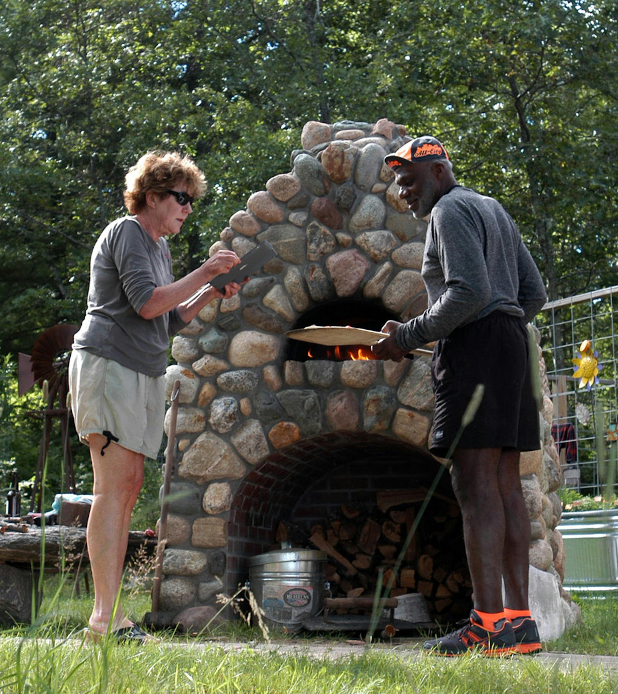 Diane and Alan Page bake pizzas in their outdoor pizza stone oven. Diane is taking a picture of the fresh pizza out of the oven.