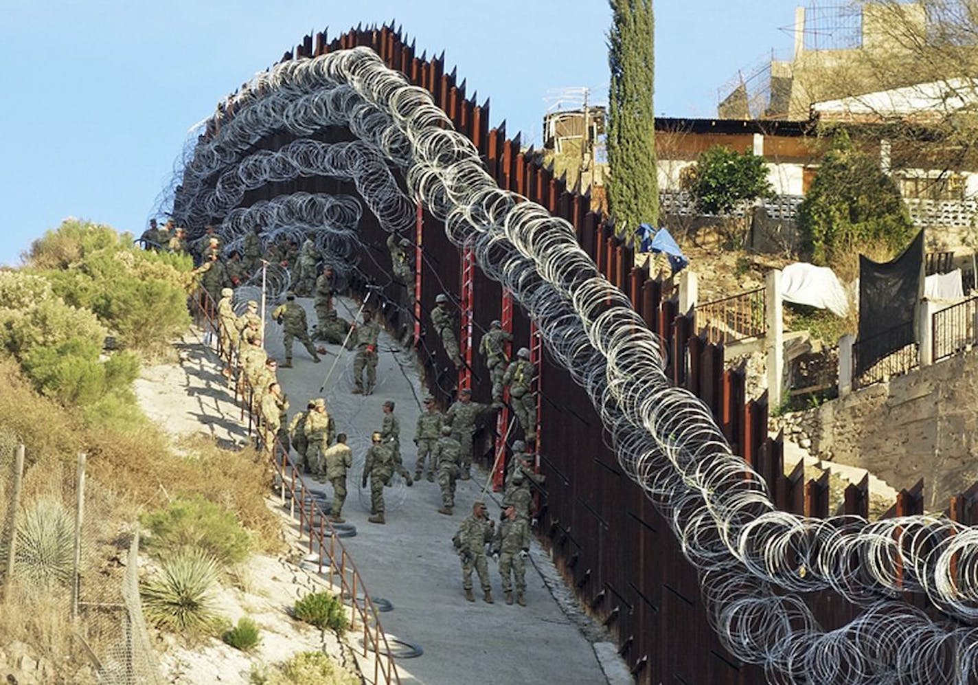 In this Saturday, Feb. 2, 2019 photo, U.S. Army troops place additional concertina wire to the border fence on a hillside above Nelson Street in downtown Nogales, Ariz. Nogales, Mexico is seen at right. The small Arizona border city is fighting back against the installation of razor fencing that now covers the entirety of a tall border fence along the city's downtown area. The city of Nogales, which sits on the border with Nogales, Mexico, is contemplating a proclamation Wednesday, Feb. 6, 2019,