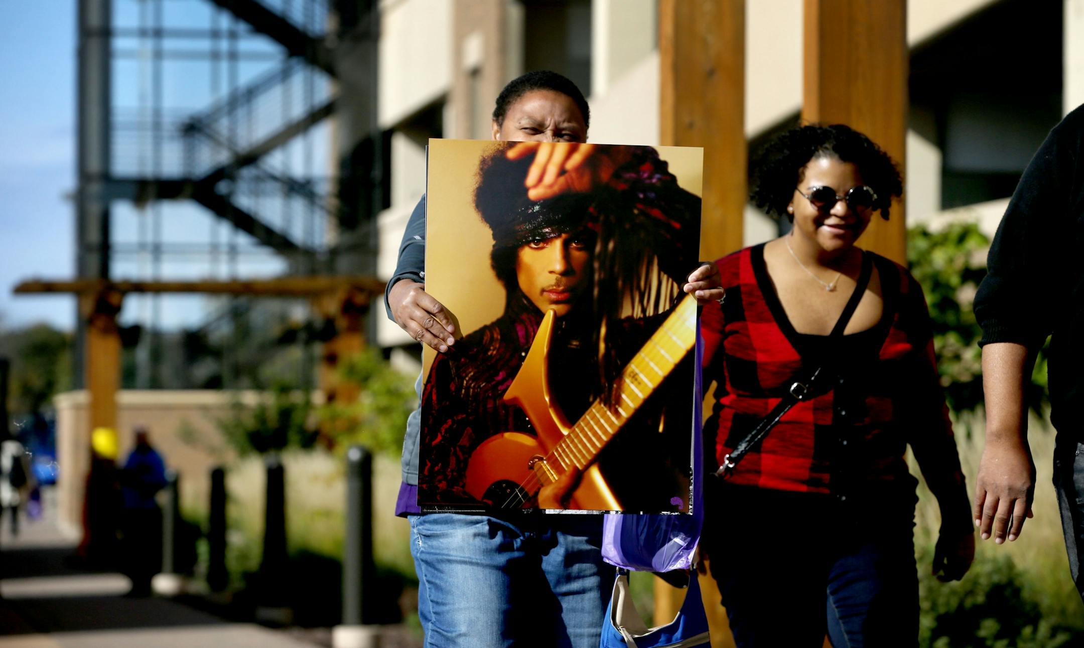 Gwen Ghess of Plymouth holds one of the Prince posters she bought during the first Paisley Park Tour as she walks from the Southwest Transit Center with her daughter Deja, right, and husband Tim, not pictured Thursday, Oct. 6, 2016, in Chanhassen, MN. "God gave us the gift of Prince," Tim said was evident after touring Paisley Park.