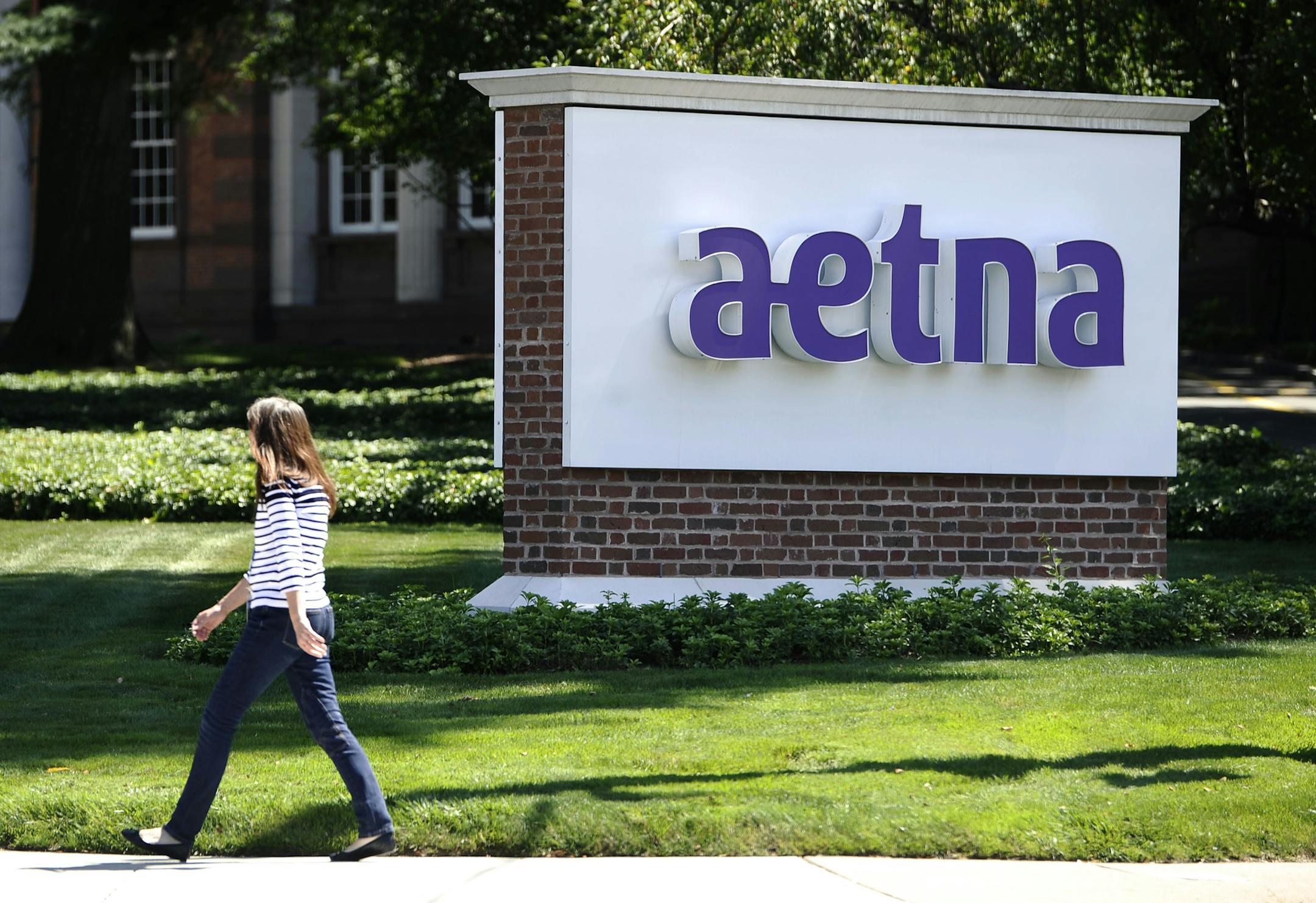 FILE - In this Tuesday, Aug. 19, 2014 file photo, pedestrian walks past a sign for health insurer Aetna Inc., at the company headquarters in Hartford, Conn. A new program from Aetna and Newtopia, a small Canadian company that creates personalized health-improvement programs, uses data from initial wellness program steps like physicals or blood tests to figure out which employees are vulnerable to metabolic syndrome. (AP Photo/Jessica Hill, File)