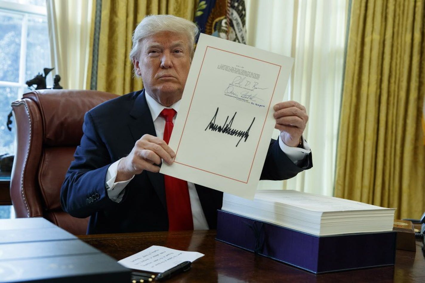 President Donald Trump shows off the tax bill after signing it in the Oval Office of the White House, Friday, Dec. 22, 2017, in Washington.