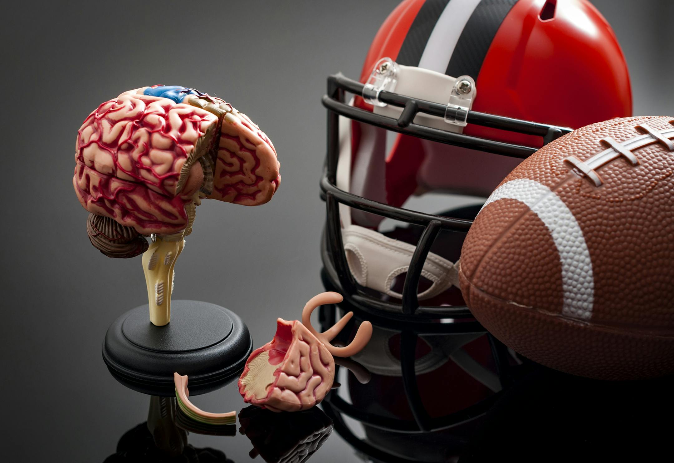 Brain damage and sports injury concept with damaged brain model, american football helmet and a ball, illustrating CTE (Chronic traumatic encephalopathy) a syndrome caused by repeated concussion