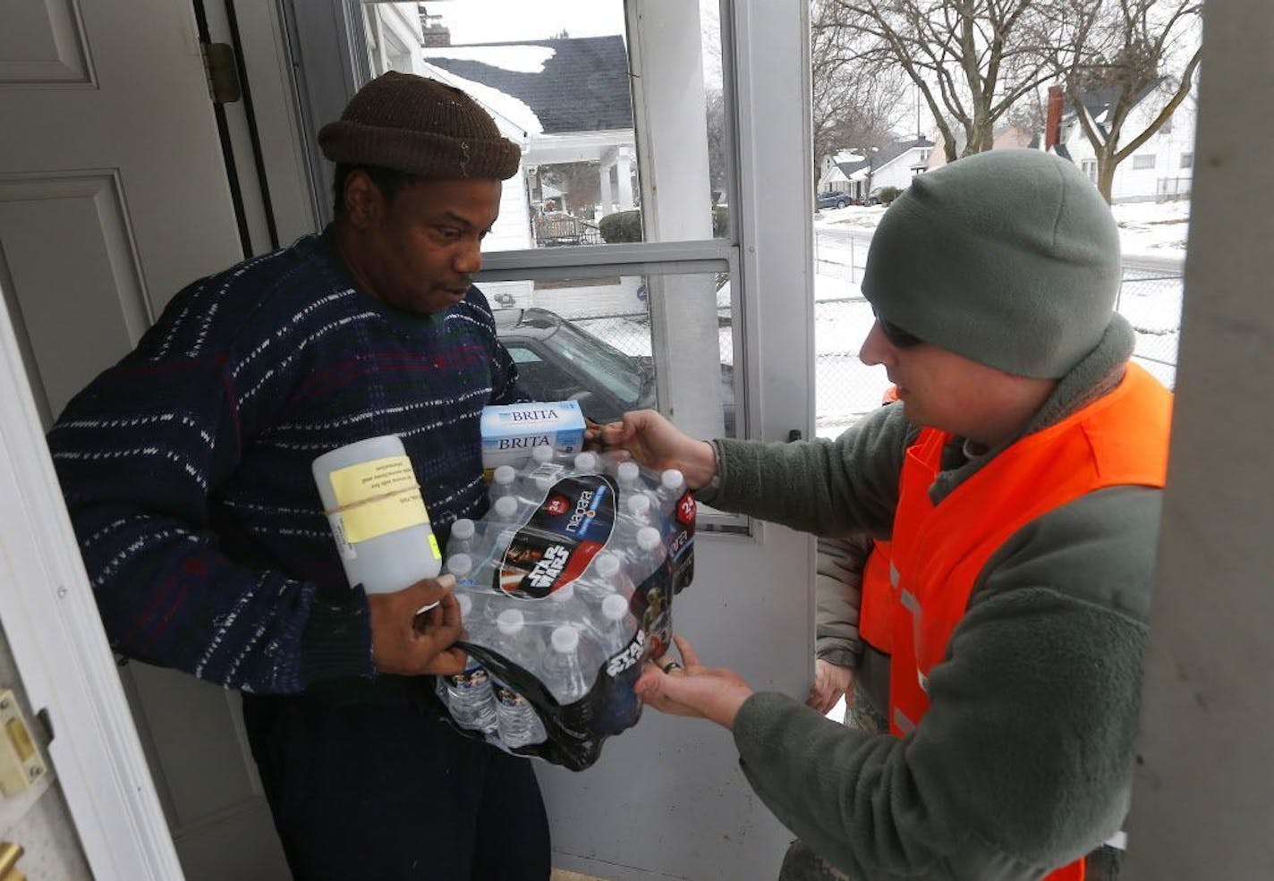 Louis Singleton receives water filters, bottled water and a test kit from Michigan National Guard Specialist Joe Weaver as clean water supplies are distributed to residents, Thursday, Jan. 21, 2016 in Flint, Mich. The National Guard, state employees, local authorities and volunteers have been distributing lead tests, filters and bottled water during the city's drinking water crisis.