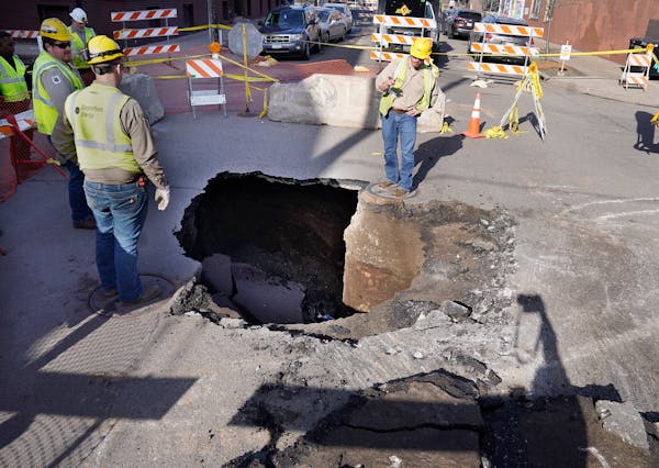 Utility workers on Monday surround a sinkhole that opened up in the middle of the intersection of W. 27th Street and Girard Avenue S.
