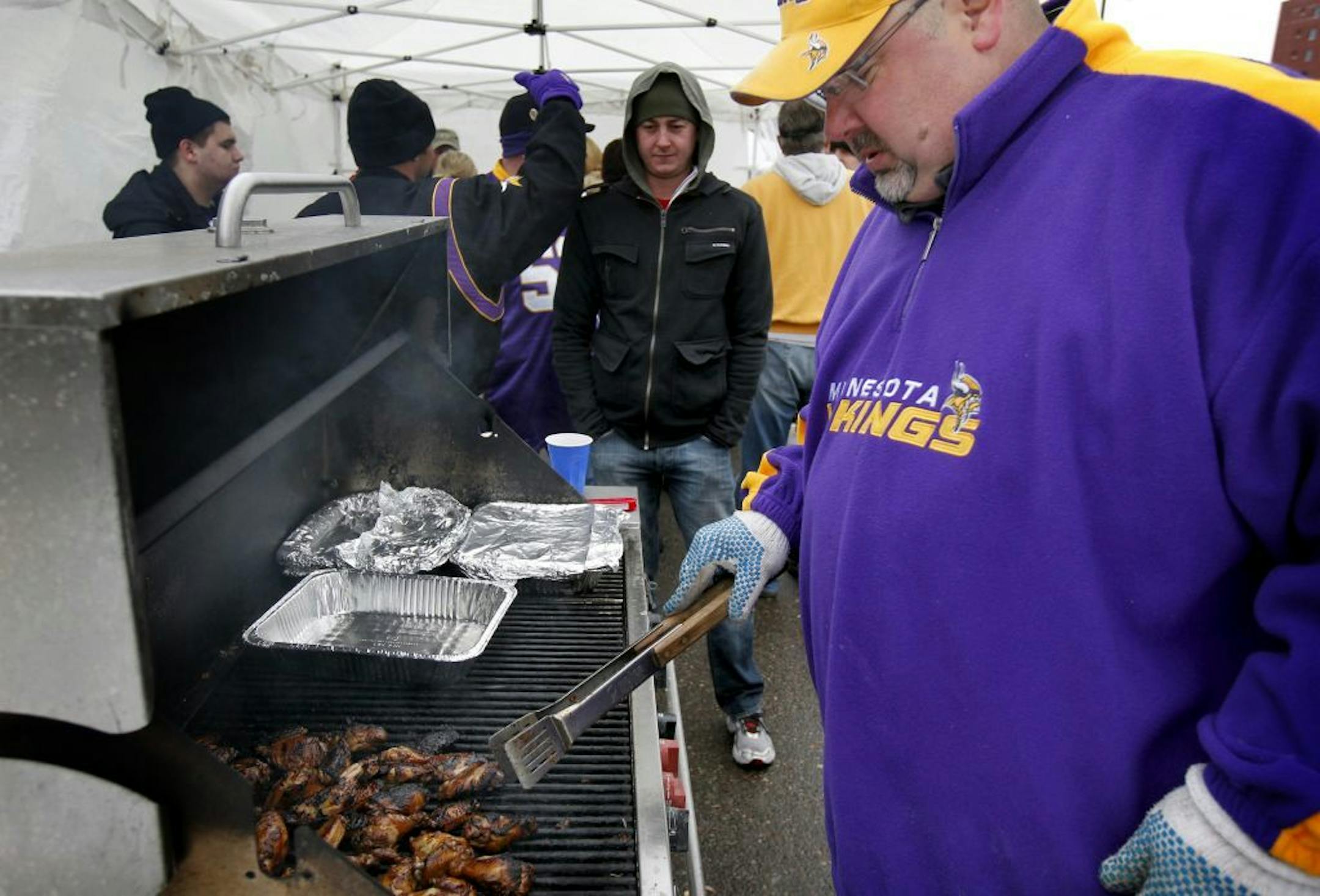 Paul Thielman (left) checked food on the grill as he tailgated with friends before Sunday's game. The group has been together for many years. The Van they use to tailgate from is called �Minks Nest� after the owner David �Mink� Minkkinen.