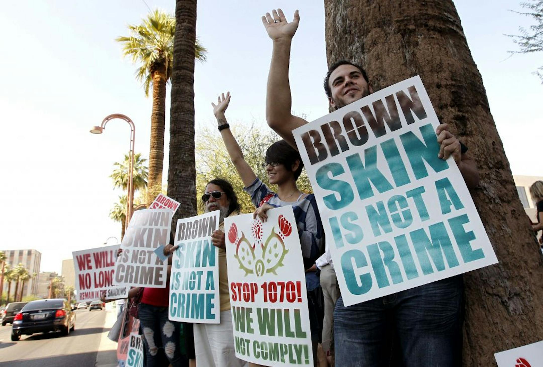 Laurent Taillefer, right, and Andrea Begay, second from right, both of Phoenix, wave at cars as they honk their horns driving by as the two join immigration rights protesters as they gather after the United States Supreme Court decision regarding Arizona's controversial immigration law, SB1070, at the local U.S. Immigration and Customs Enforcement offices Monday, June 25, 2012, in Phoenix. The Supreme Court struck down key provisions of Arizona�s crackdown on immigrants Monday but said a much-de