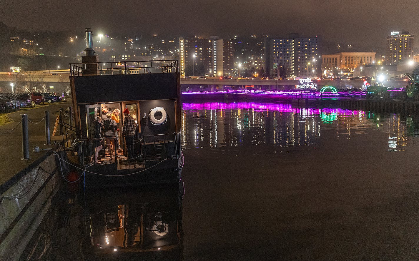 With the Duluth skyline in the background, Neil Rasmussen, the general manager for Duluth experience, leads clients into the Cedar and Stone's new sauna barge near Pier B, in Duluth, Minn., on Saturday, Dec. 16, 2023.