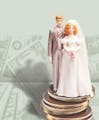 200 dpi 63p x 77p Rick Nease color illustration of a bride and groom wedding cake figurine set on a stack of coins against a background of money. Detr