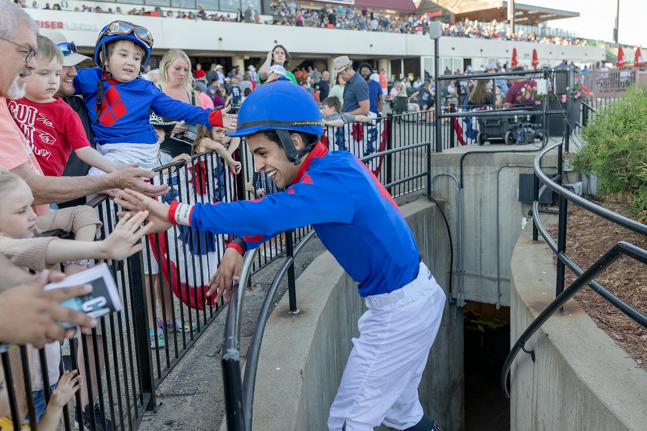 Young fan Austin Erickson, being held by his father Jake, reaches out to congratulate his favorite Jockey Carlos Ulloa after a victory during a race.