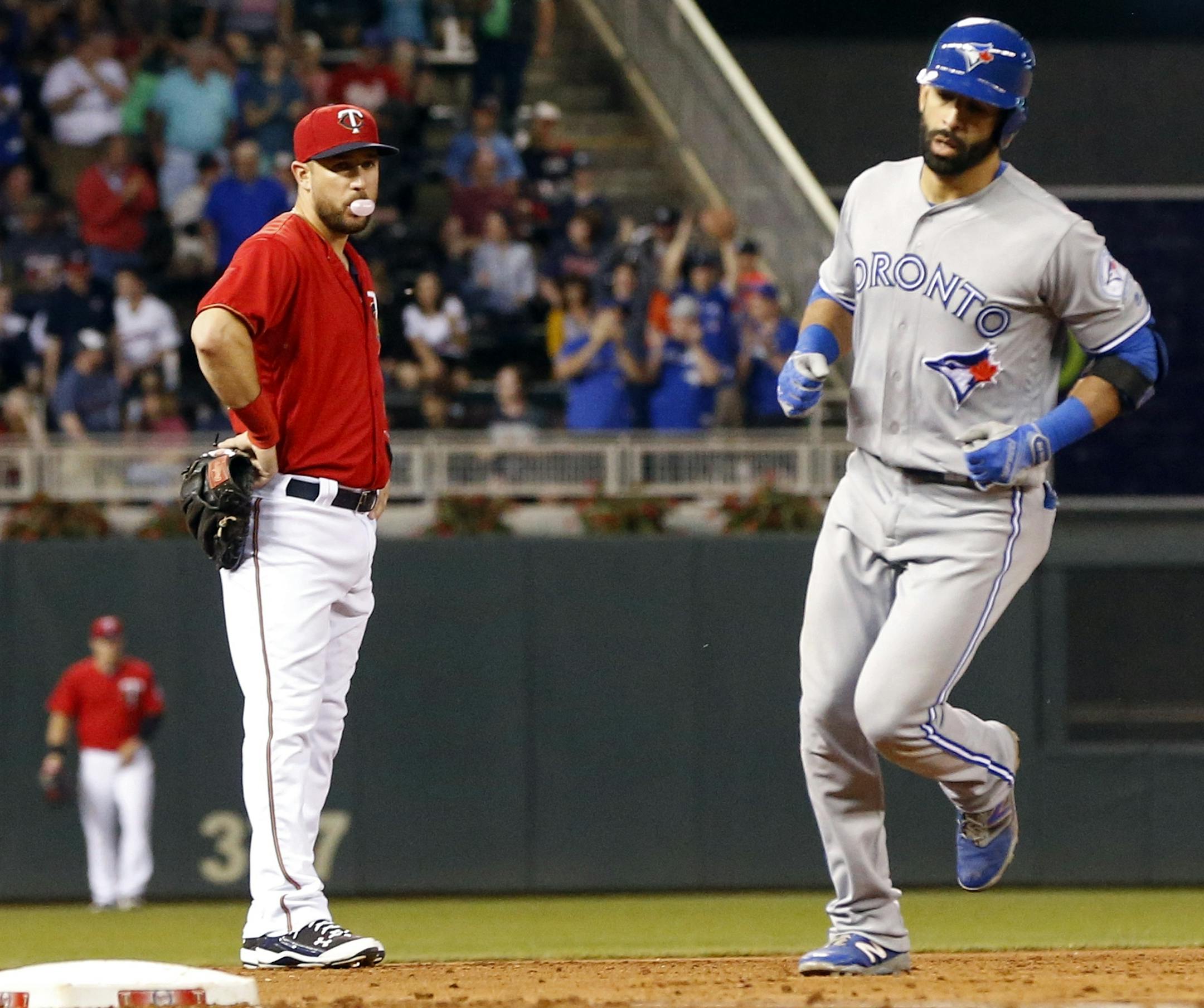Minnesota Twins third baseman Trevor Plouffe, left, blows a bubble as Toronto Blue Jays’ Jose Bautista rounds third on his three-run home run off Minnesota Twins pitcher Trevor May in the sixth inning of a baseball game Friday, May 20, 2016, in Minneapolis. (AP Photo/Jim Mone)