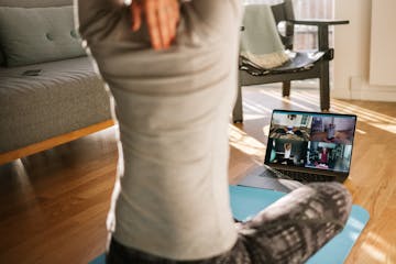 Fitness coach teaching yoga online to group of people. Yoga trainer demonstrating yoga poses to students via video conference.