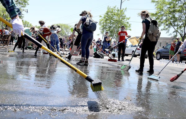A small army of community members and volunteers work to clear water and debris outside 27 Avenue Cafe, just off of Lake Street, damaged by agitators 