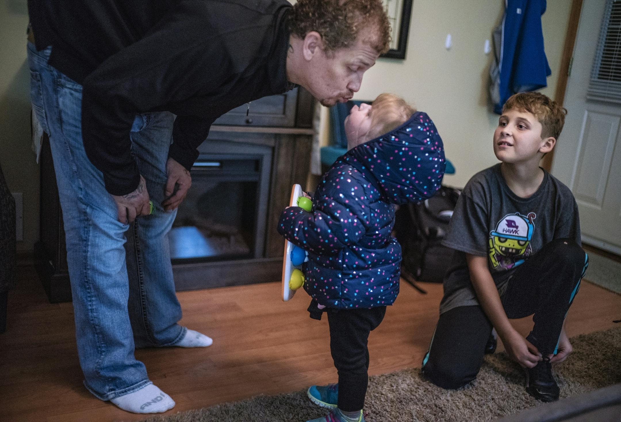 Alex Kempe gives a kiss to his youngest Sabriella,2, while Aiden,9 ties his shoes and gets ready to go back to his mother's house.