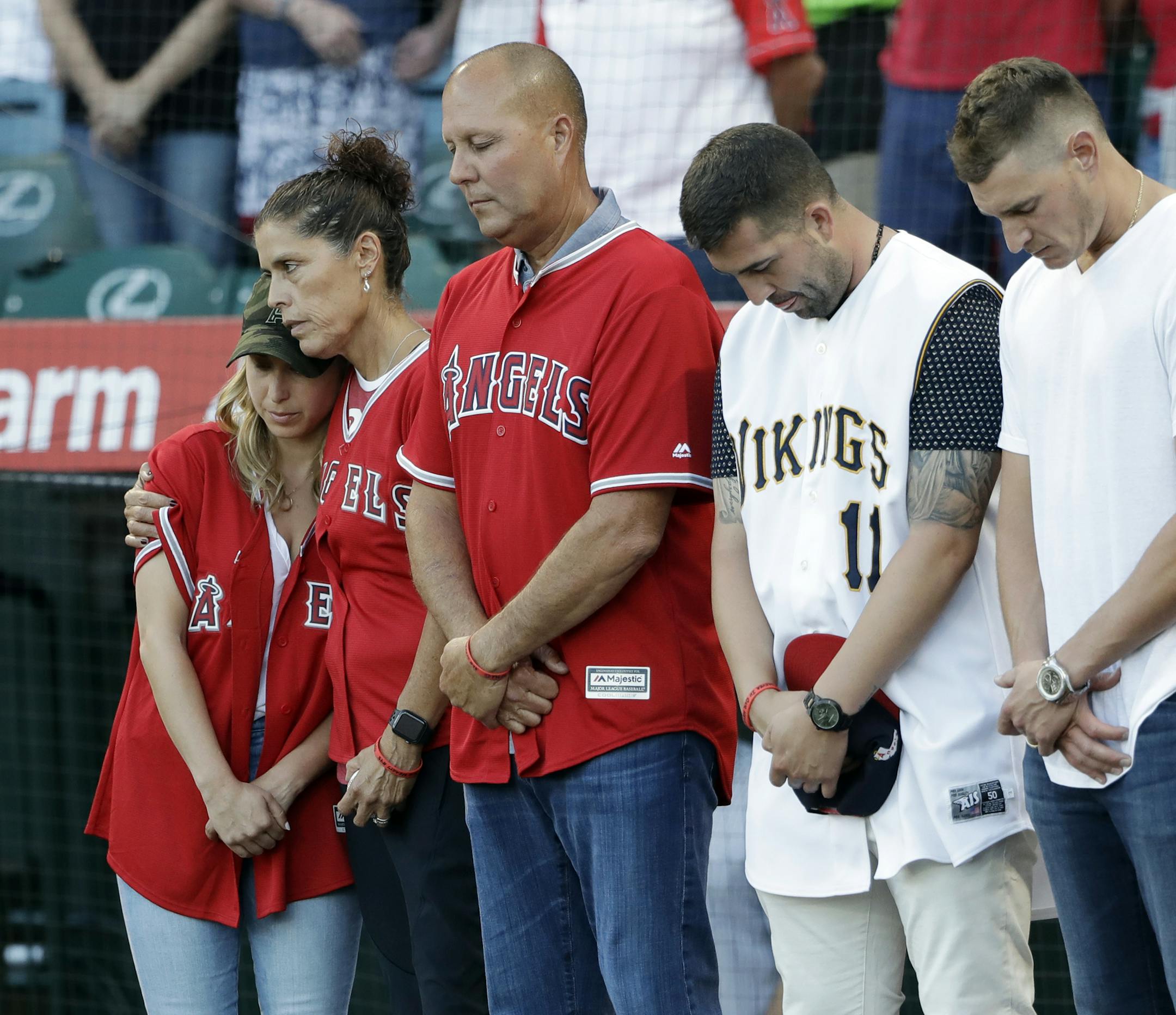 CORRECTS MOTHER'S LAST NAME TO HETMAN, INSTEAD OF SKAGGS - CORRECTS NAME OF PERSON AT MIDDLE - Members of Tyler Skaggs' family, including wife, Carli, left; mother, Debbie Hetman, second from left; and Danny Hetman, third from left, join in a moment of silence in Tyler's honor before the Los Angeles Angels' baseball game against the Seattle Mariners on Friday, July 12, 2019, in Anaheim, Calif. (AP Photo/Marcio Jose Sanchez)